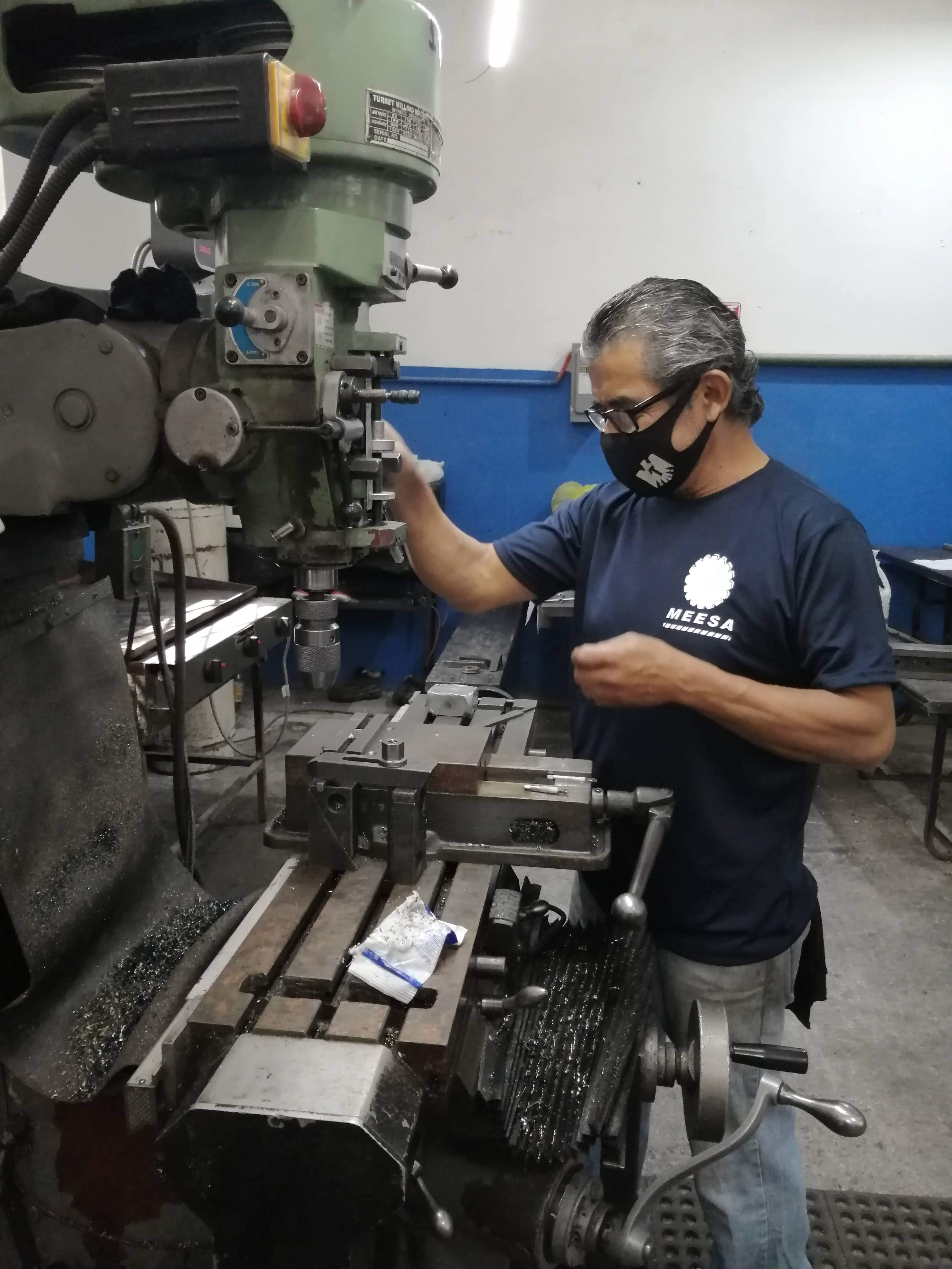 Hombre operando una máquina industrial en un taller, usando una mascarilla protectora.