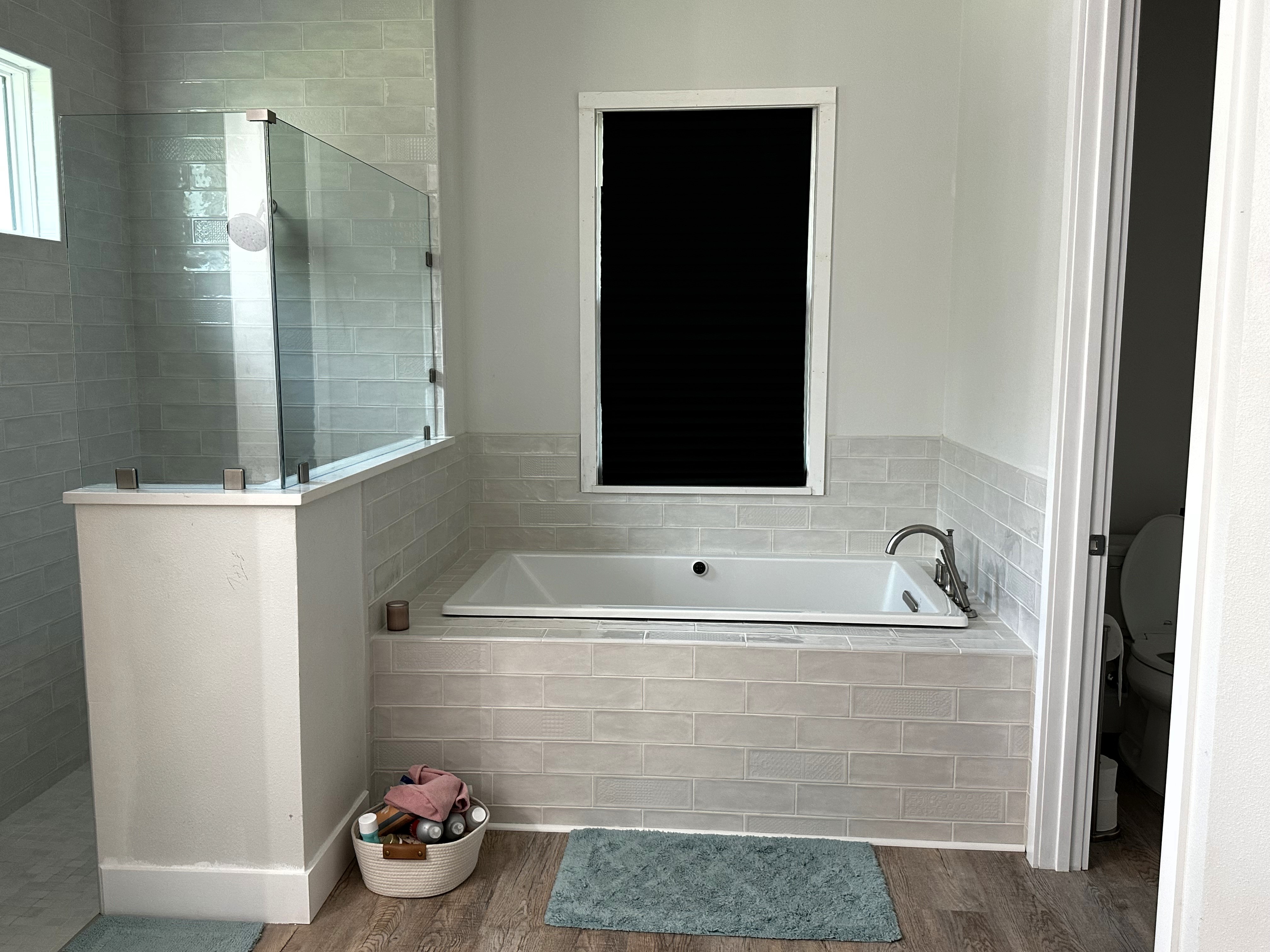 Light & bright primary bathroom with large soaking tub, separate walk-in shower featuring heavy clear glass panels with clips, and 4x12 White Deco tiles.  