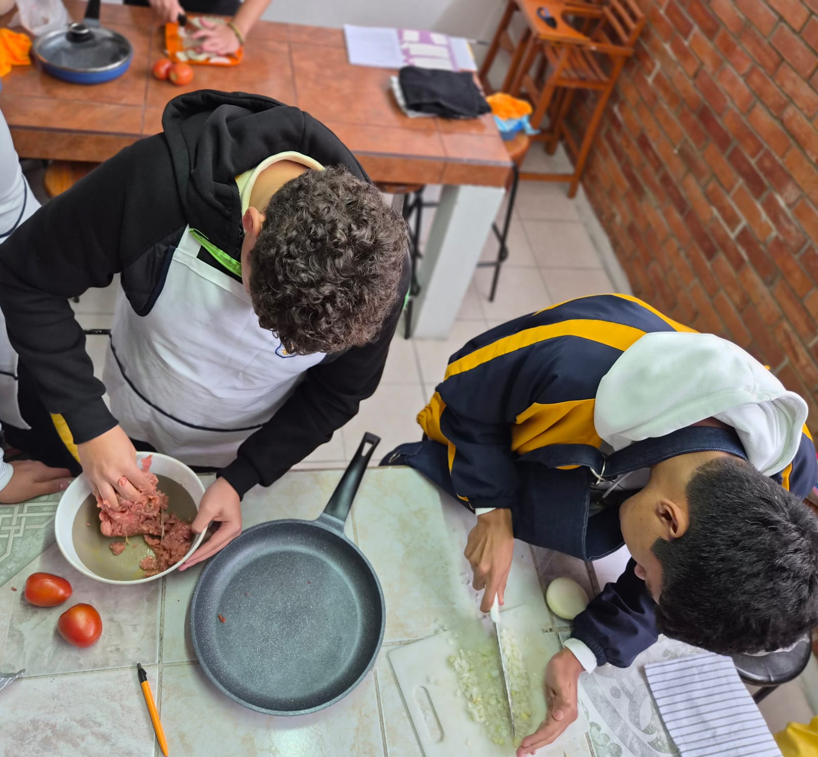 Reunión de grupo en oficina con laptop mostrando pantalla, personas sonriendo y conversando alrededor de mesa de madera con iluminación moderna.