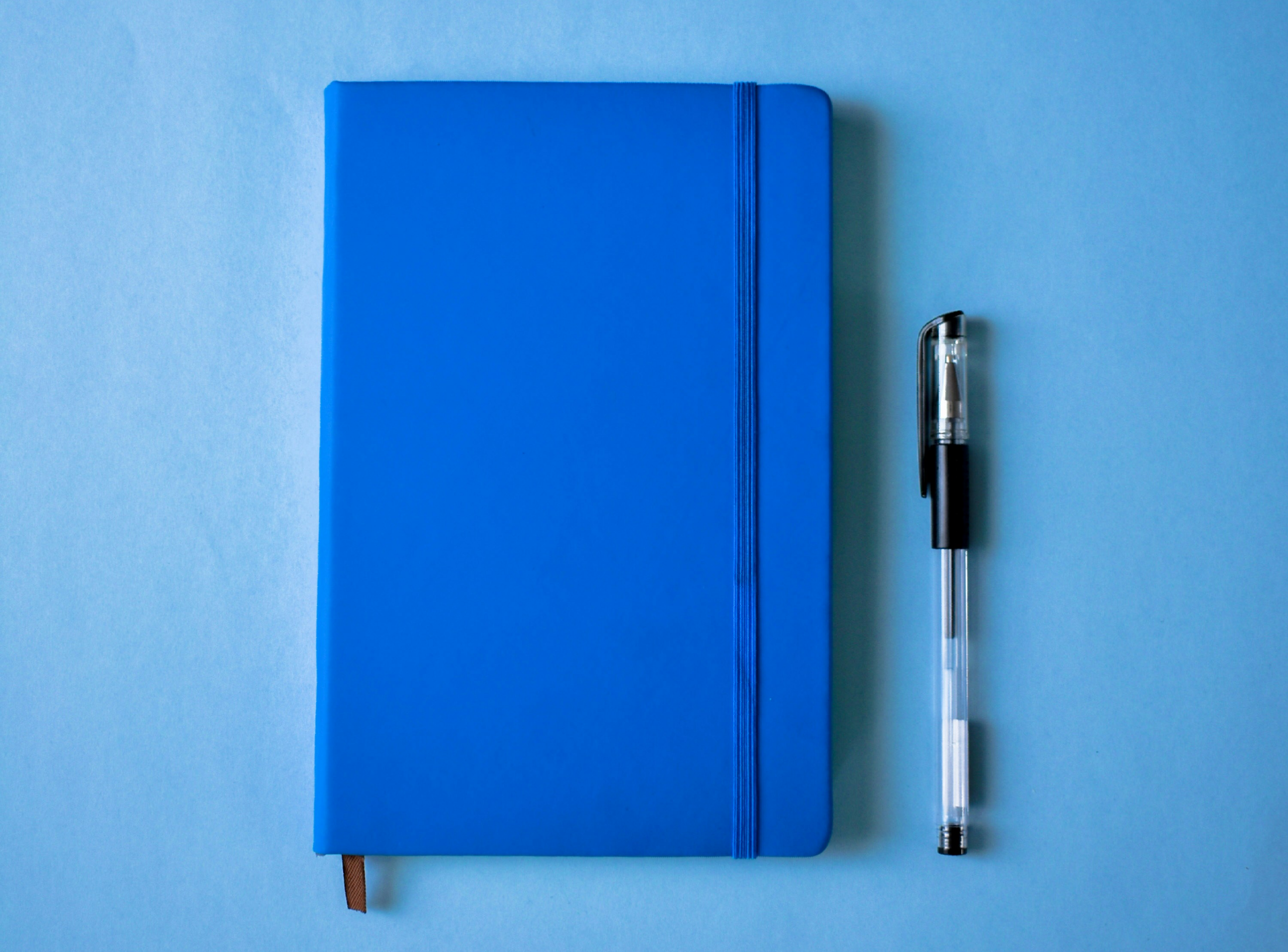 Cuaderno azul con bolígrafo sobre fondo azul claro.