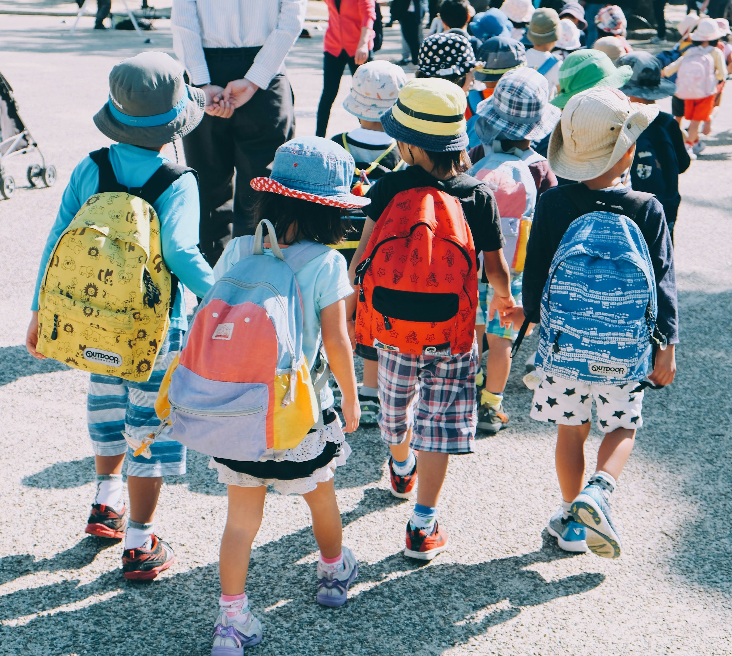 group of people wearing white and orange backpacks walking on gray concrete pavement during daytime
