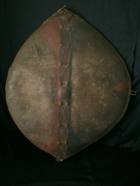 PRODUCT PROFILE :
Product No. : #21297
Description :  Massai Warrior Shield
PRODUCT NARRATIVE :
• Buffalo hide, red and black
    paint.
• This old shield has warped
     edge on warriors right side.
• Battle scars sword or spear
    on hide with period wire 
     repair.
• Circa: 1900, Size: 36" x 24"