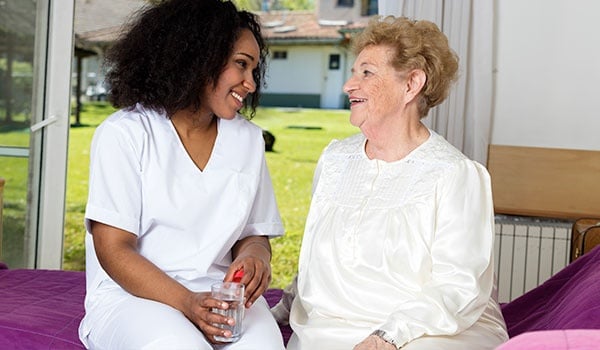 Nurse Giving Glass of Water To Elder Woman