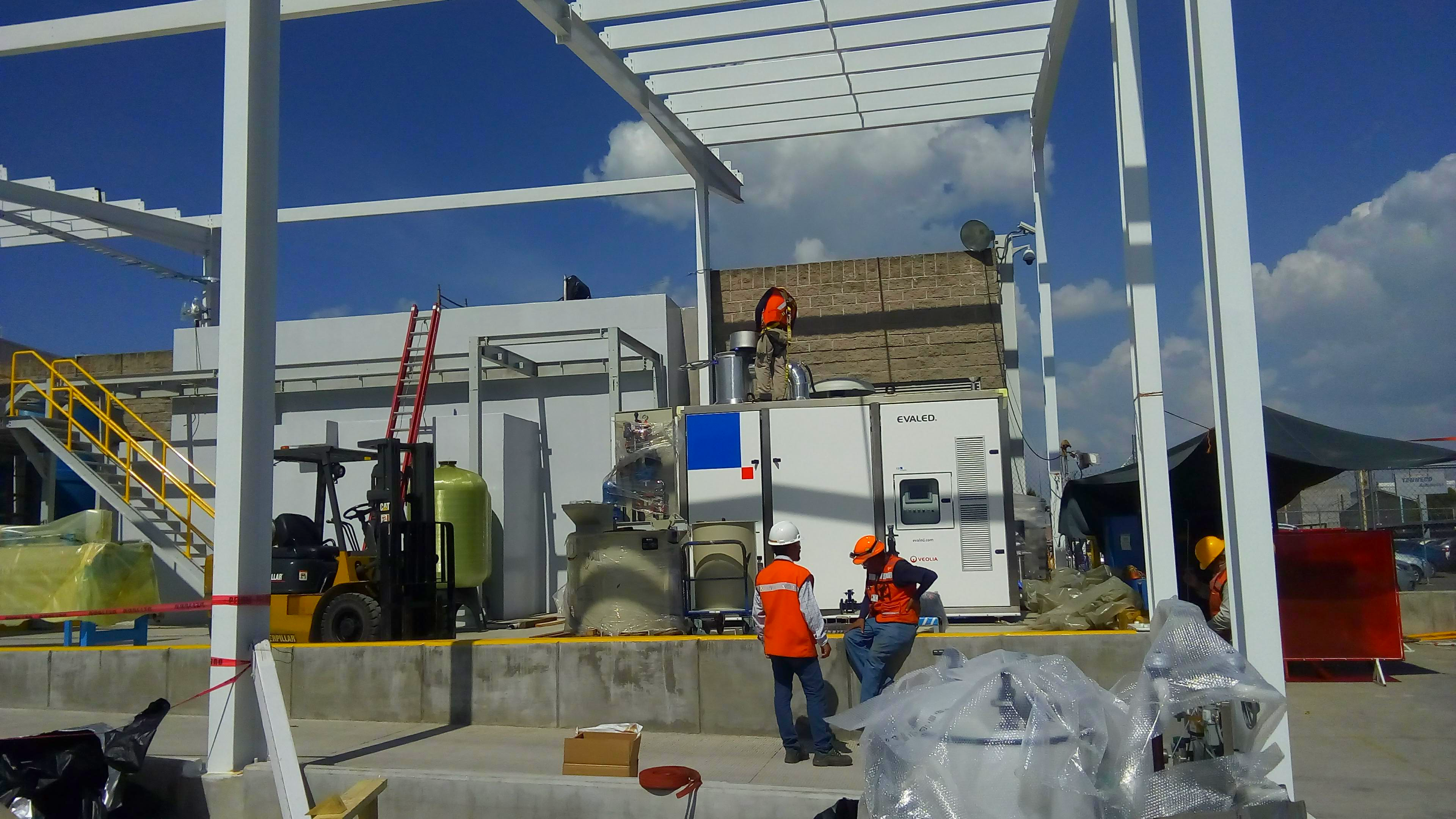 Construcción industrial con estructura metálica, montacargas y trabajadores instalando maquinaria en planta