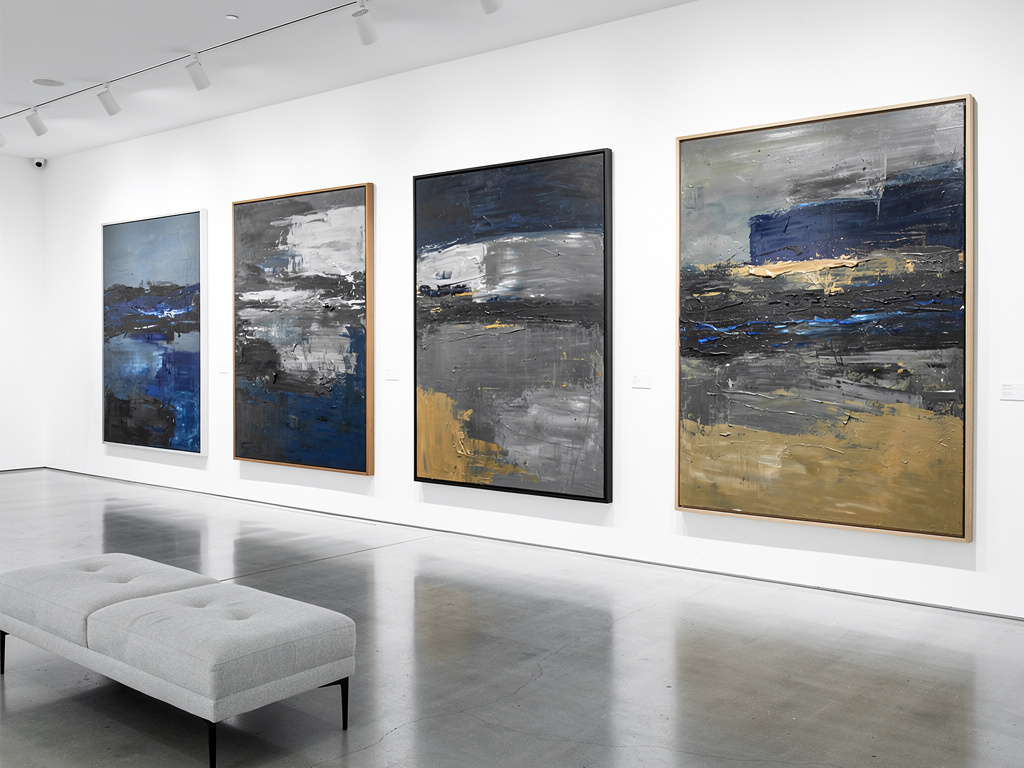 Galería de arte contemporáneo con cuatro cuadros abstractos en tonos azul, gris y dorado sobre pared blanca