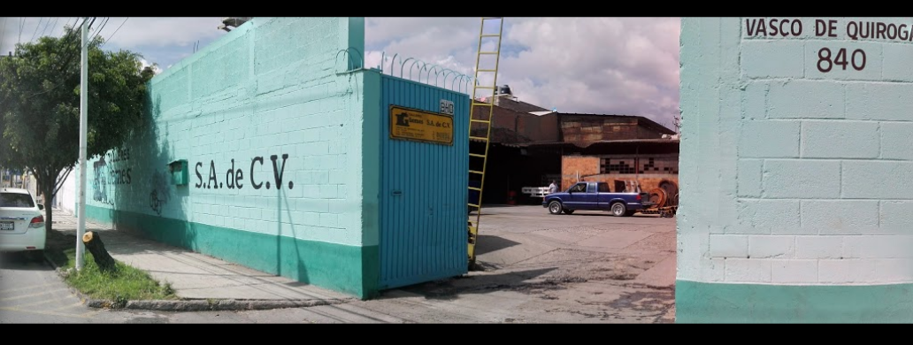 Fachada de un edificio industrial con paredes pintadas de turquesa, una puerta de entrada azul, señal de empresa S.A. de C.V., y una camioneta azul en el estacionamiento.