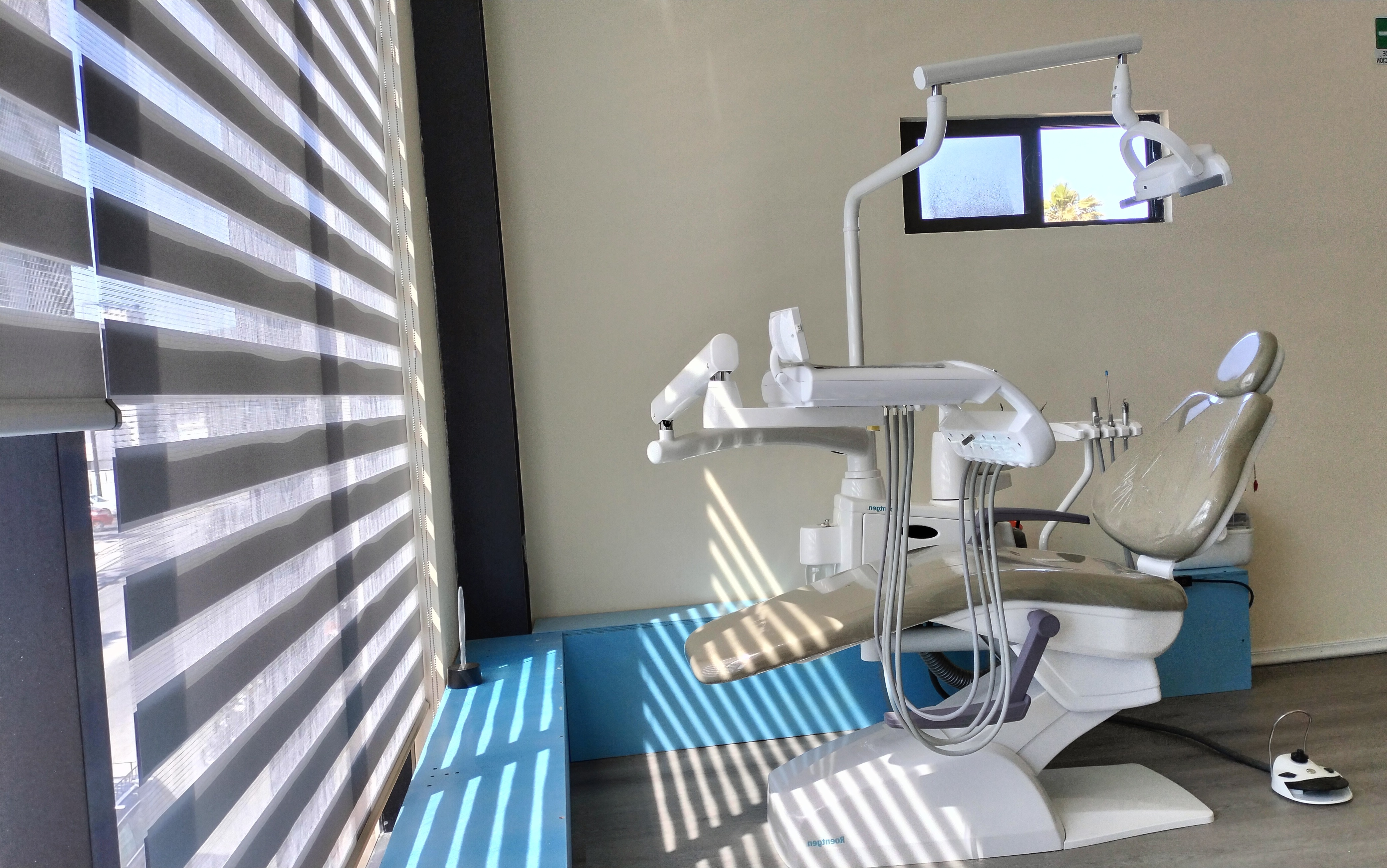Sala de dentista con silla dental gris, instrumental y ventana con cortinas.