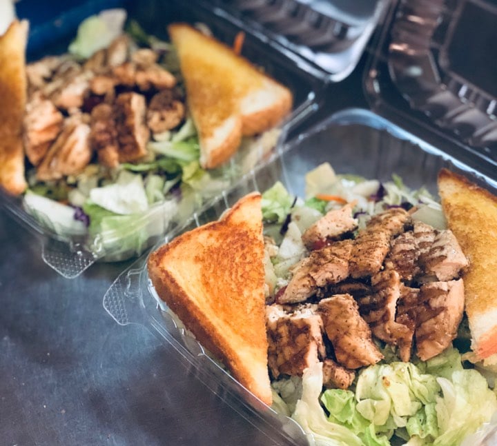 Grilled chicken salad with toasted bread triangles in plastic containers.
