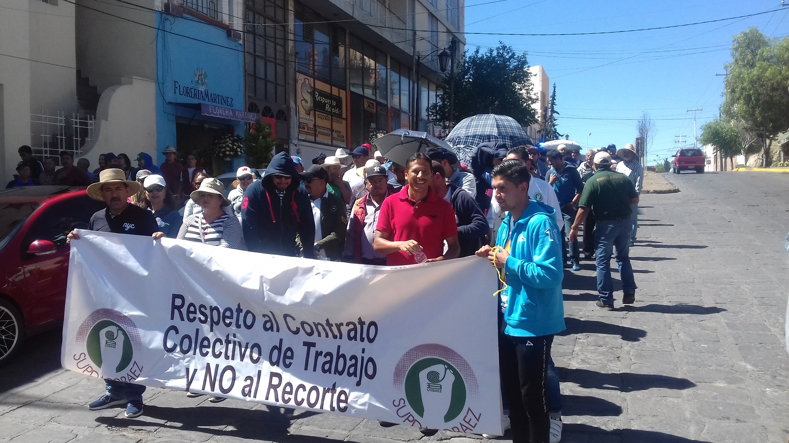Manifestación de personas en la calle sosteniendo una pancarta que dice 'Respeto al Contrato Colectivo de Trabajo y NO al Recorte', con edificios al fondo y clima soleado.