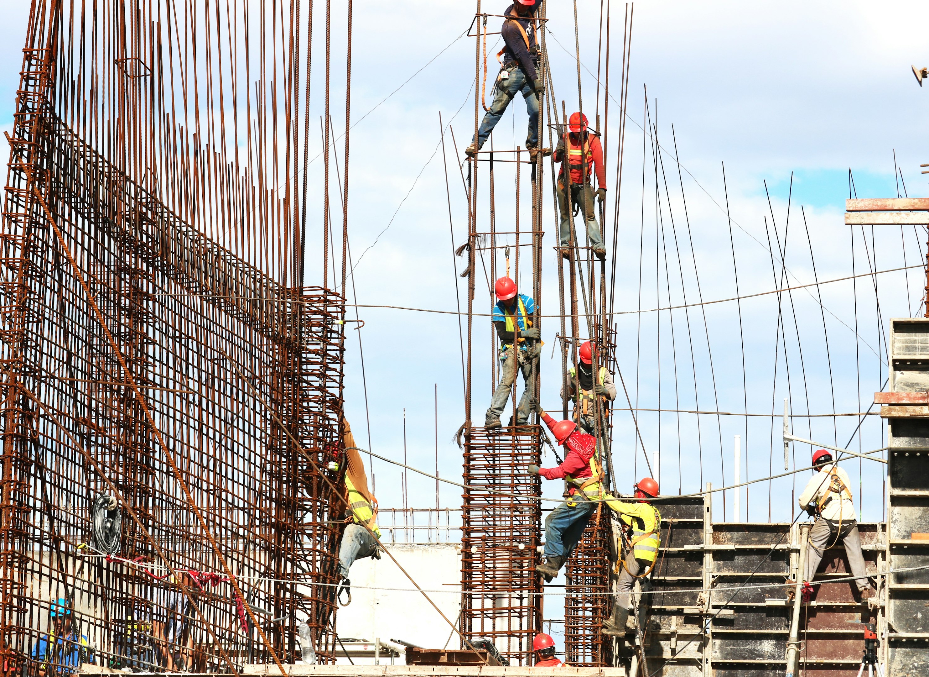 Construction workers with safety gear working on a building site with steel rods and scaffolding.