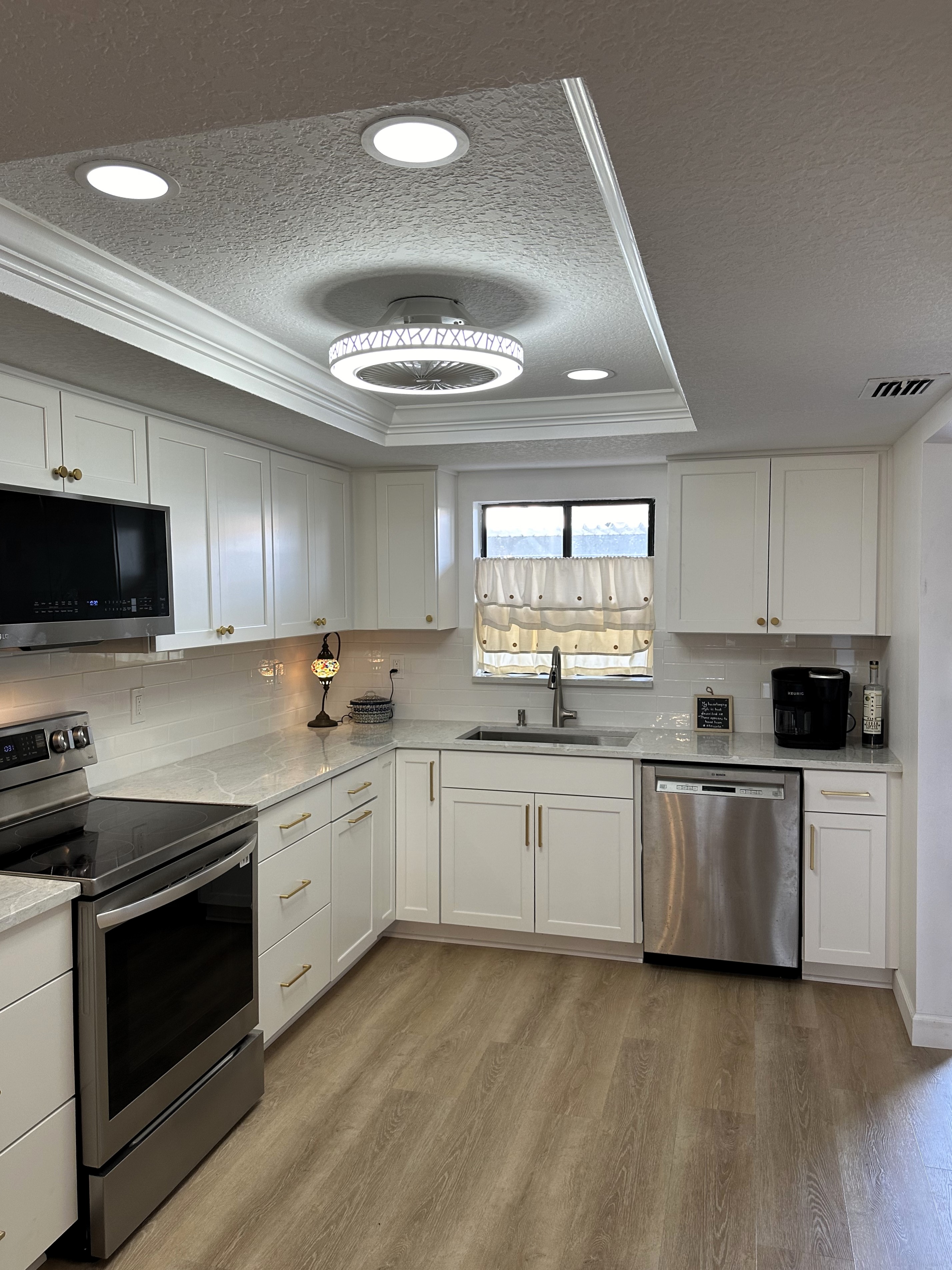 Charming kitchen featuring maple painted White semi-custom cabinetry, gold hardware, beautiful Pompeii Coastal quartz countertop, and white subway tile. 