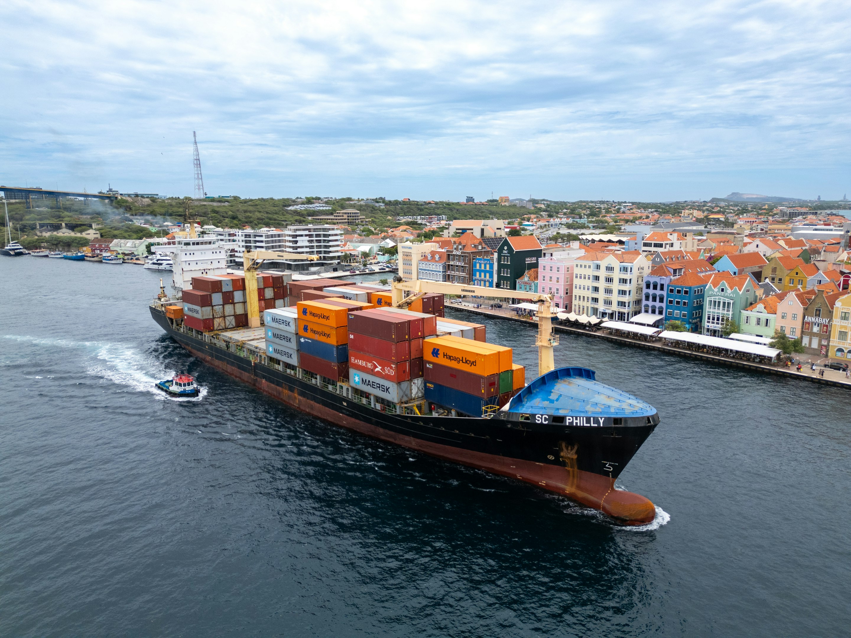 Cargo ship navigating Willemstad harbor in Curacao, with colorful waterfront buildings in the background. Cargo ship navigating Willemstad harbor in Curacao, with colorful waterfront buildings in the background.