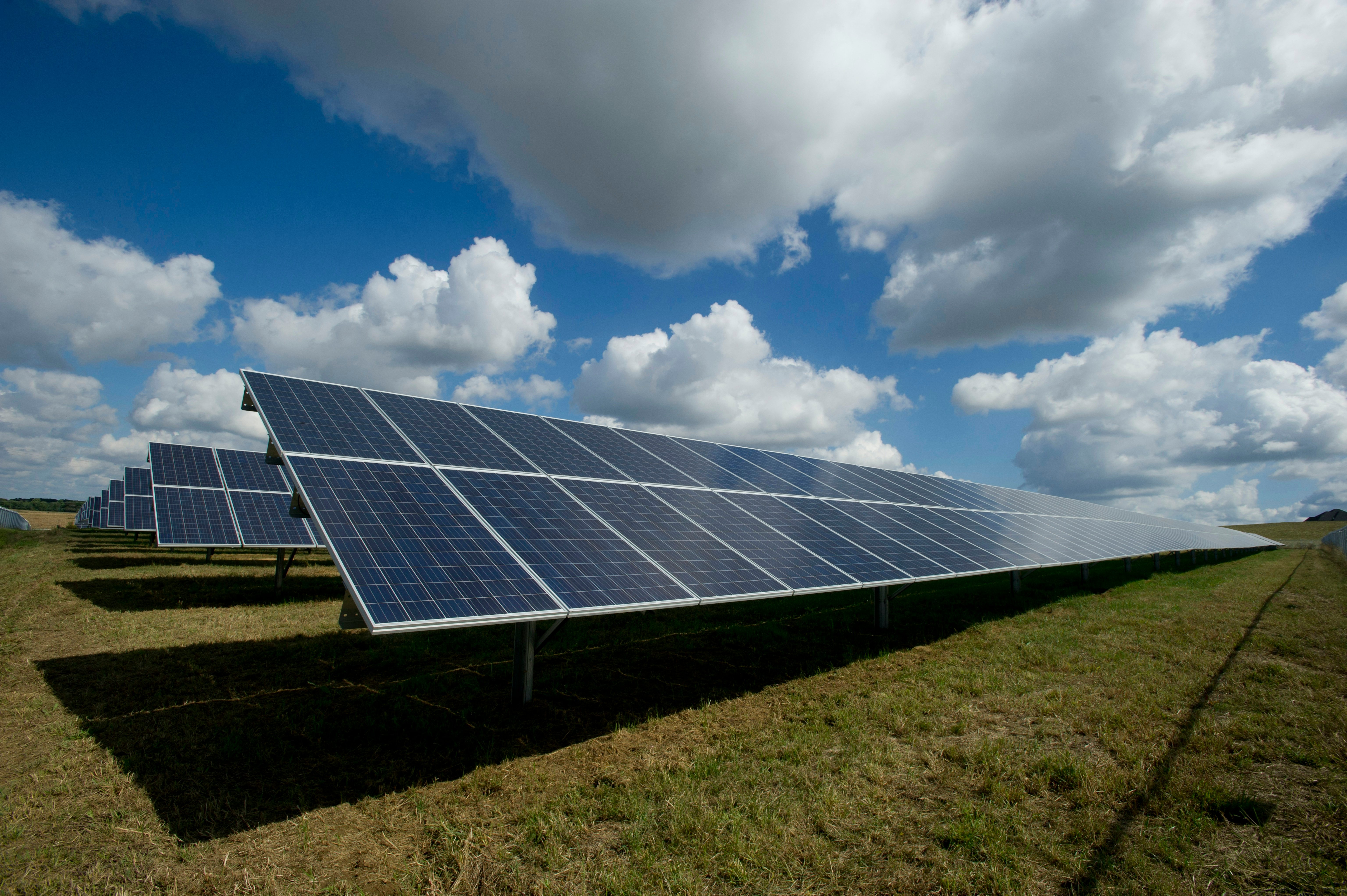 Paneles solares fotovoltaicos en campo bajo cielo azul con nubes, energía renovable sostenible