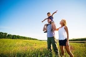 Family enjoying a sunny day in a grassy field with child riding on father's shoulders