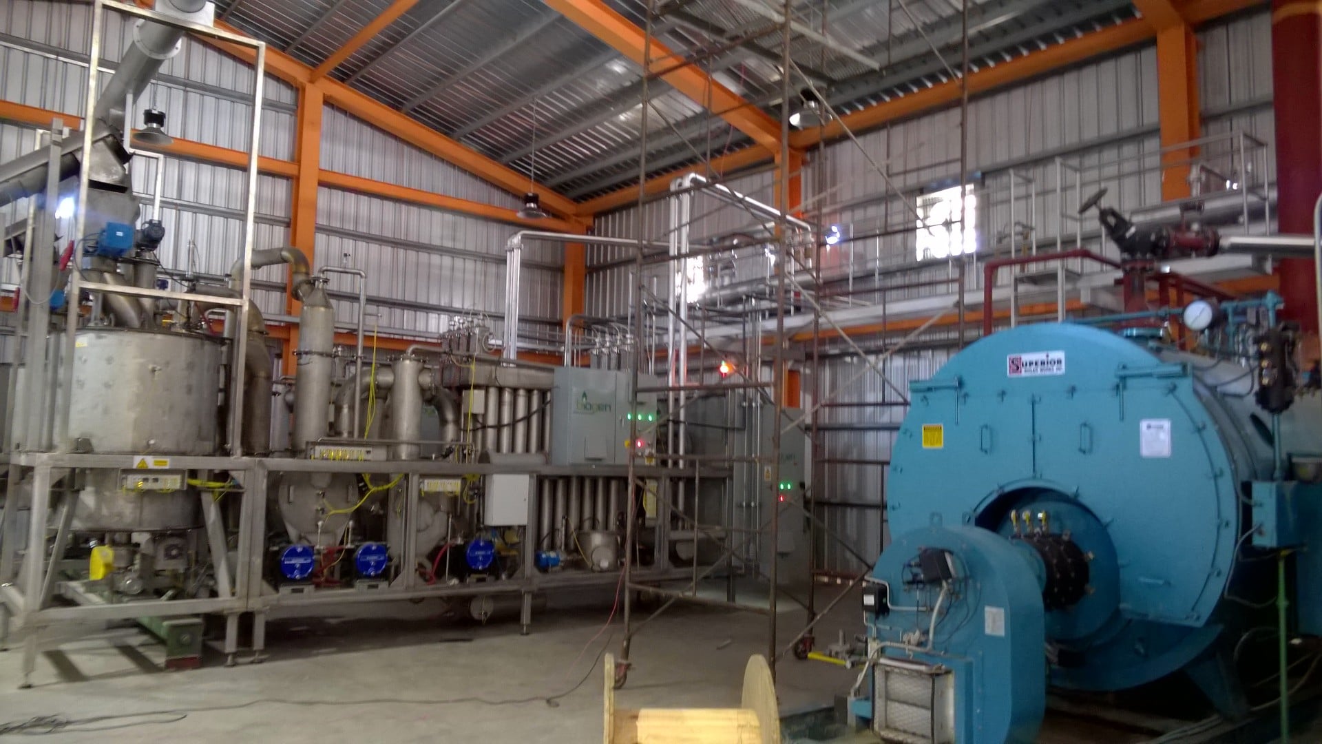 Sala industrial con caldera azul, tuberías, tanques de acero y equipos de procesamiento en una planta de producción