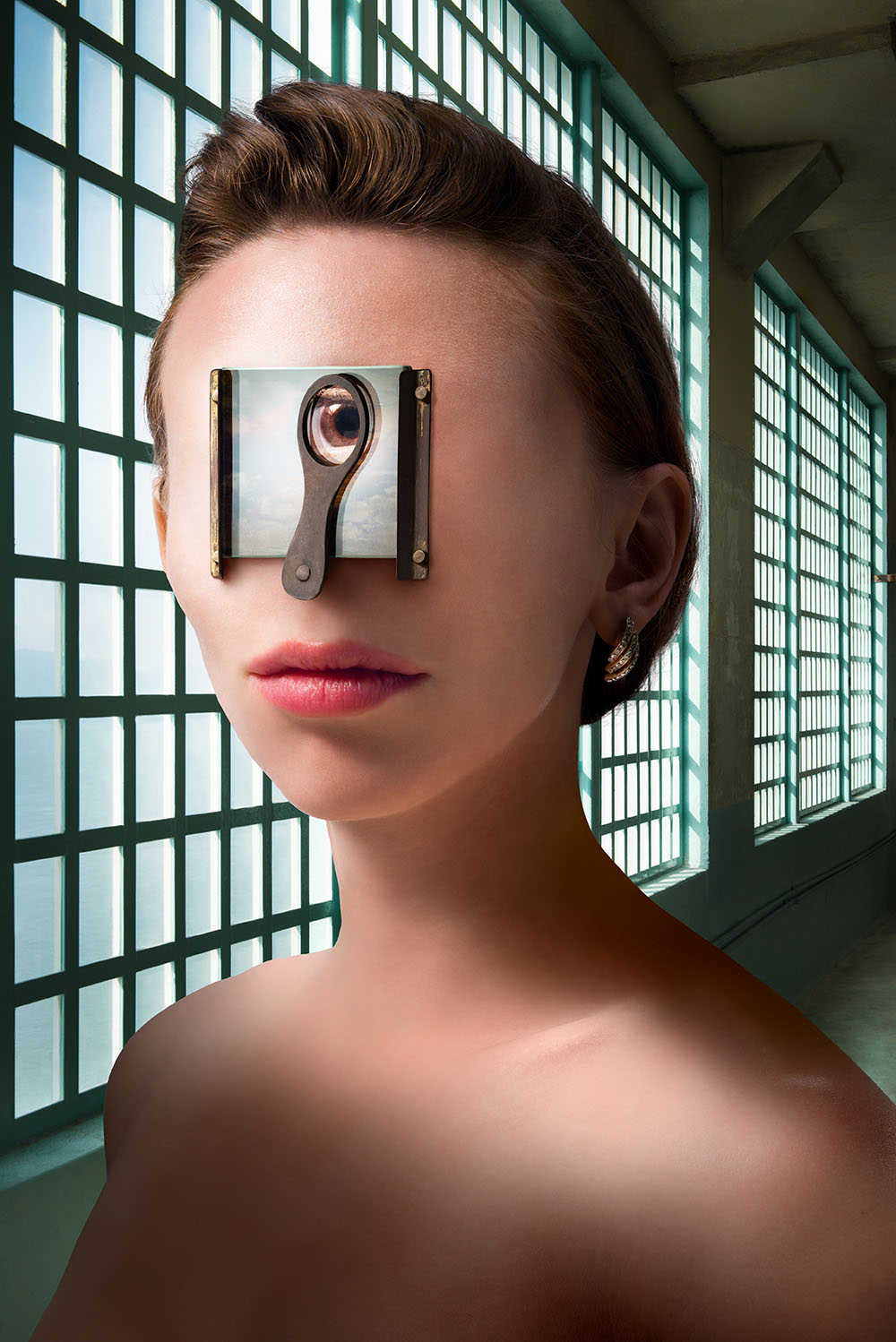 Intense, surreal portrait of woman with a single eye visible through a small glass window attached to the middle of her face. 