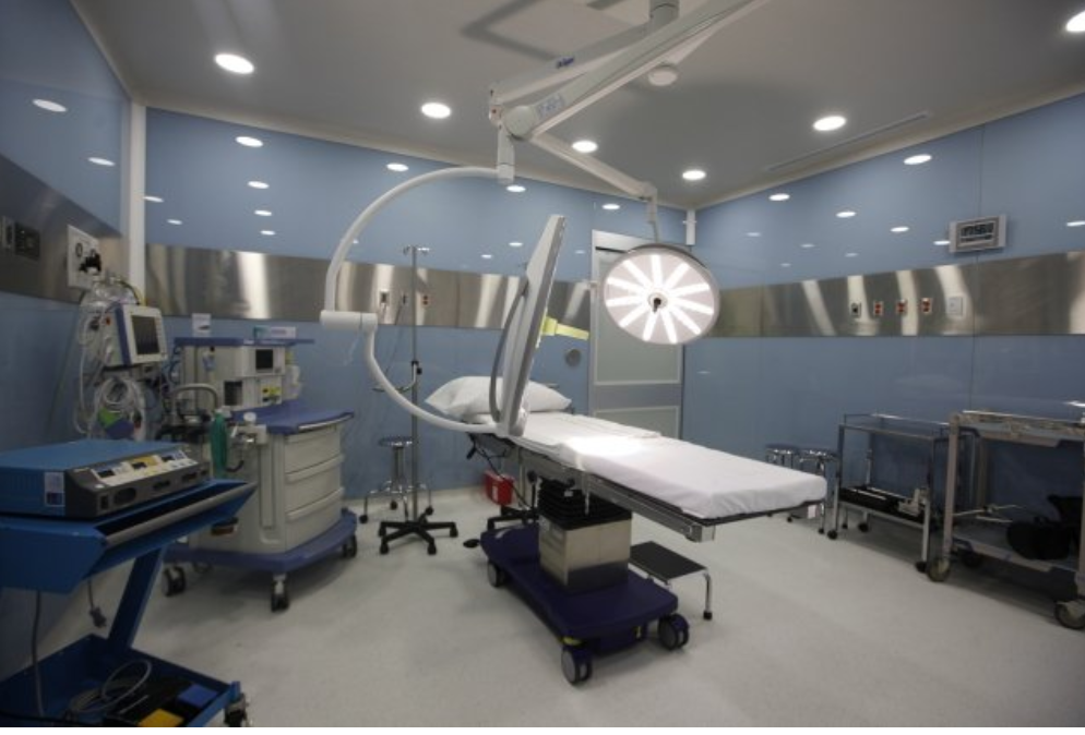 Sala de operaciones moderna con equipo médico avanzado, mesa quirúrgica, luces quirúrgicas y paredes de color azul claro.