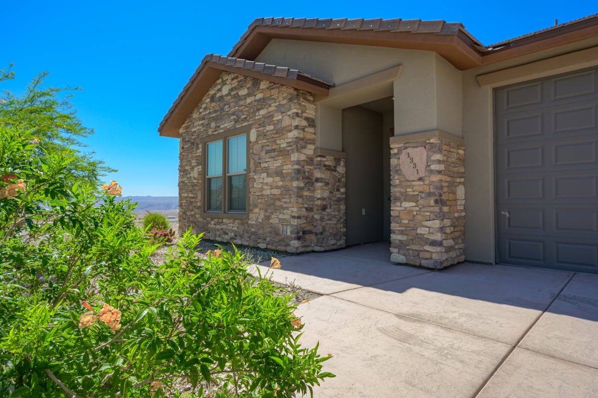 Modern suburban home exterior at dusk with stone facade, neatly landscaped yard, and illuminated pathway.