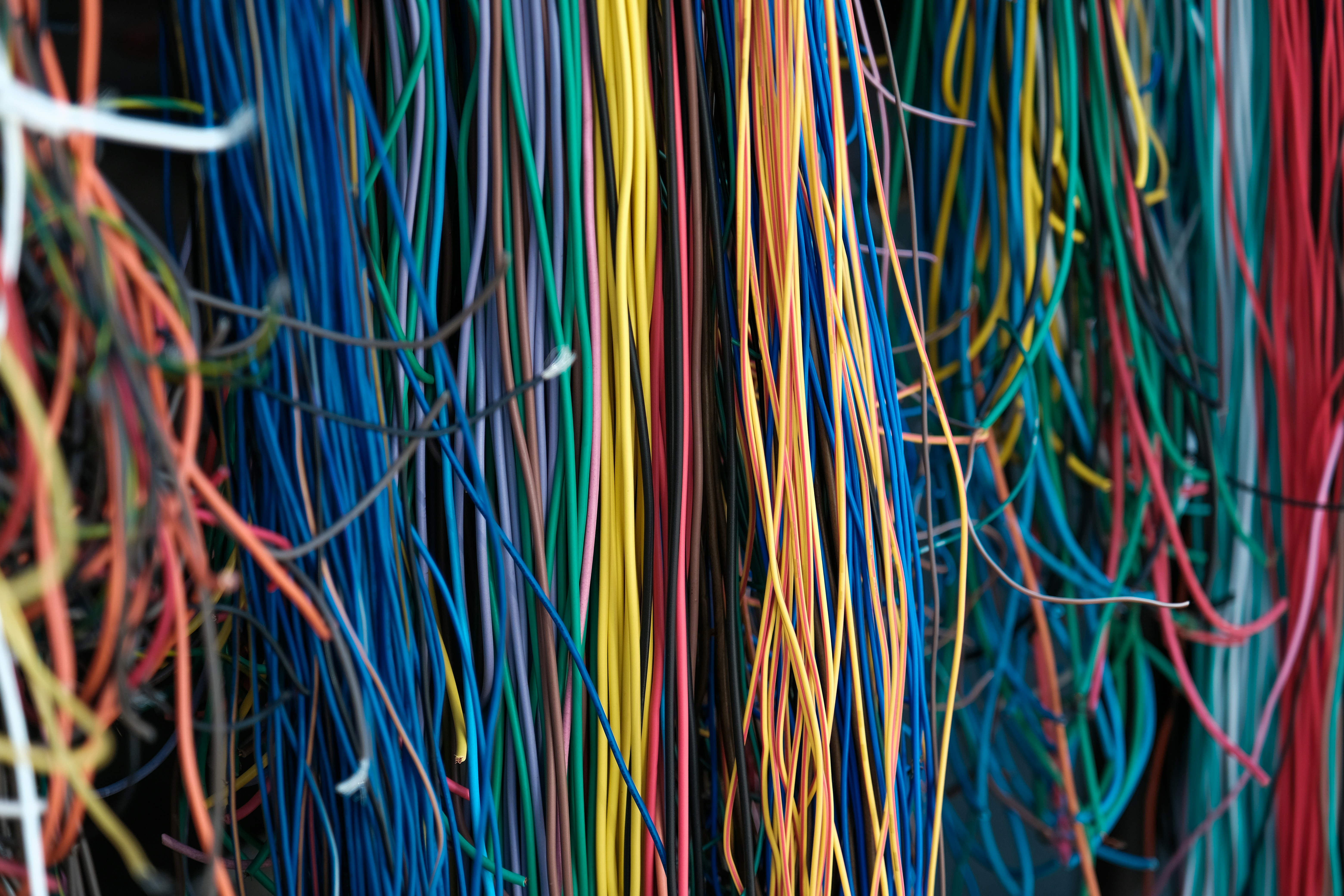 Engineer in hard hat and safety vest working on network equipment with blue cables in a server room.