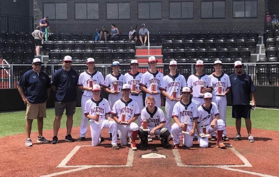 Youth baseball team in Patriots uniforms posing with trophies on a baseball field.