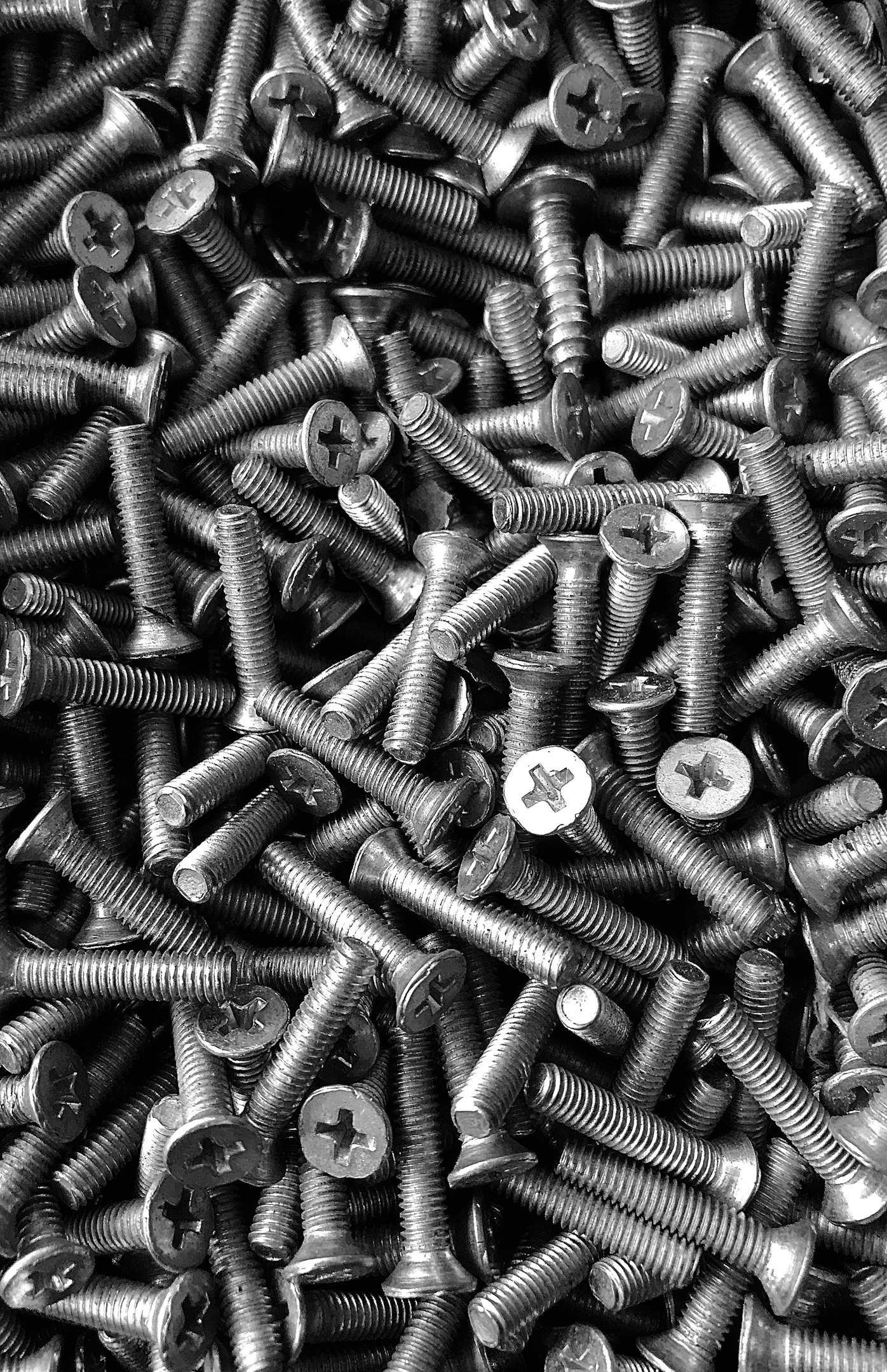 Close-up of various metal bolts and screws on a reflective surface in a well-lit workshop.
