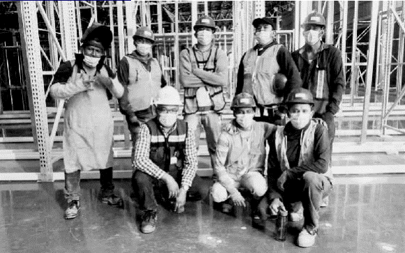 Grupo de trabajadores de la construcción con cascos y mascarillas, posando juntos en un sitio de obra con estructuras metálicas de fondo. Grupo de trabajadores de la construcción con cascos y mascarillas, posando juntos en un sitio de obra con estructuras metálicas de fondo.