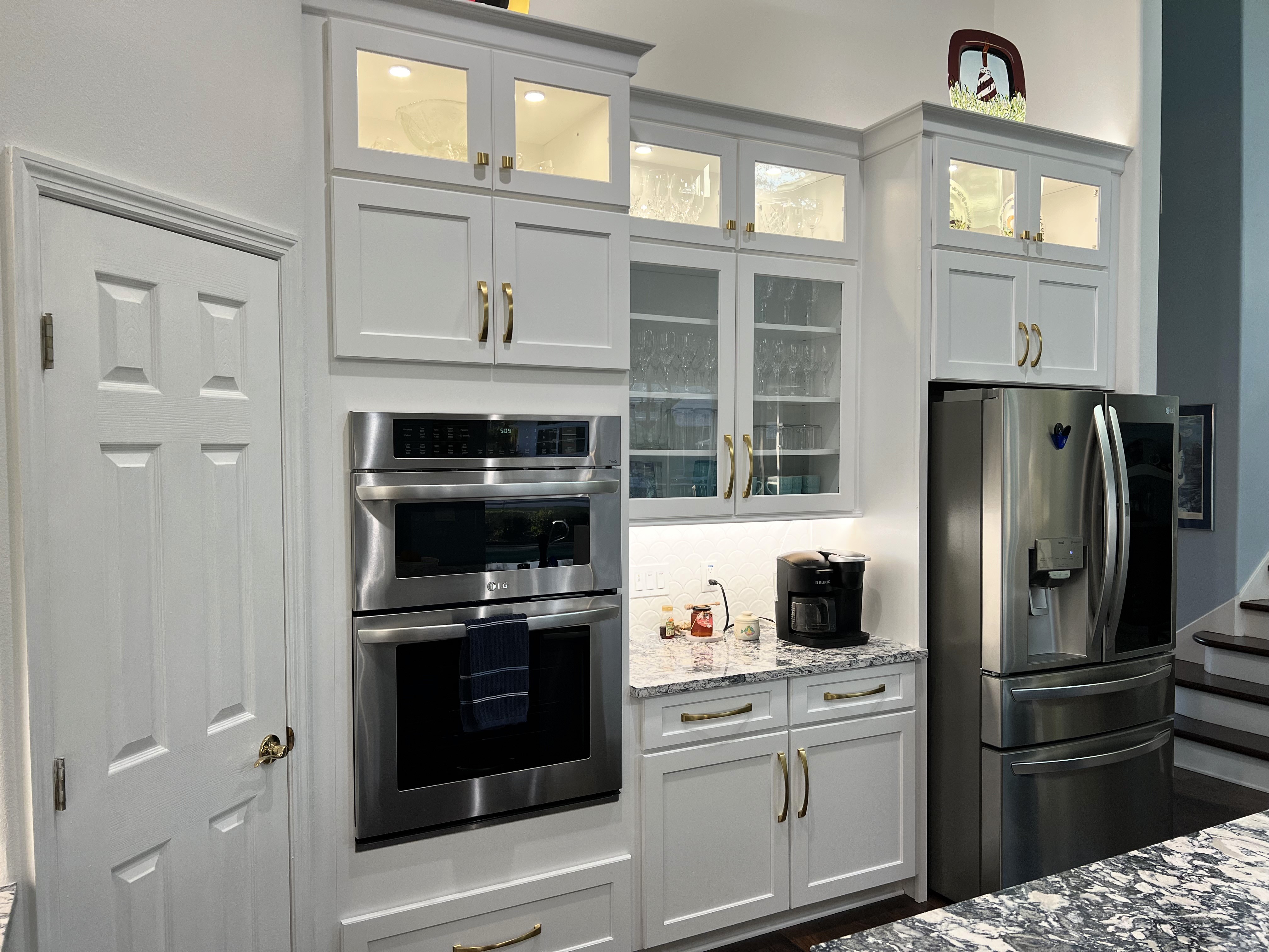 Beautifully lit stacked cabinetry featuring glass fronts with gold knobs and undercabinet lighting for the perfect coffee bar area.  