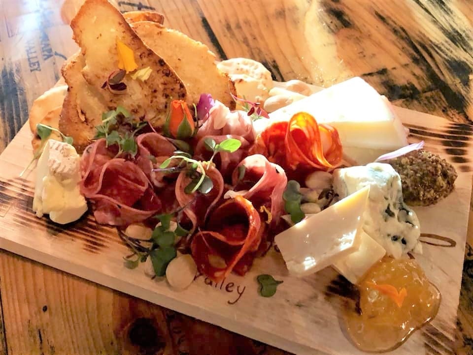 Charcuterie board with assorted cheeses, cured meats, nuts, bread slices, and fruit preserves on a wooden table.