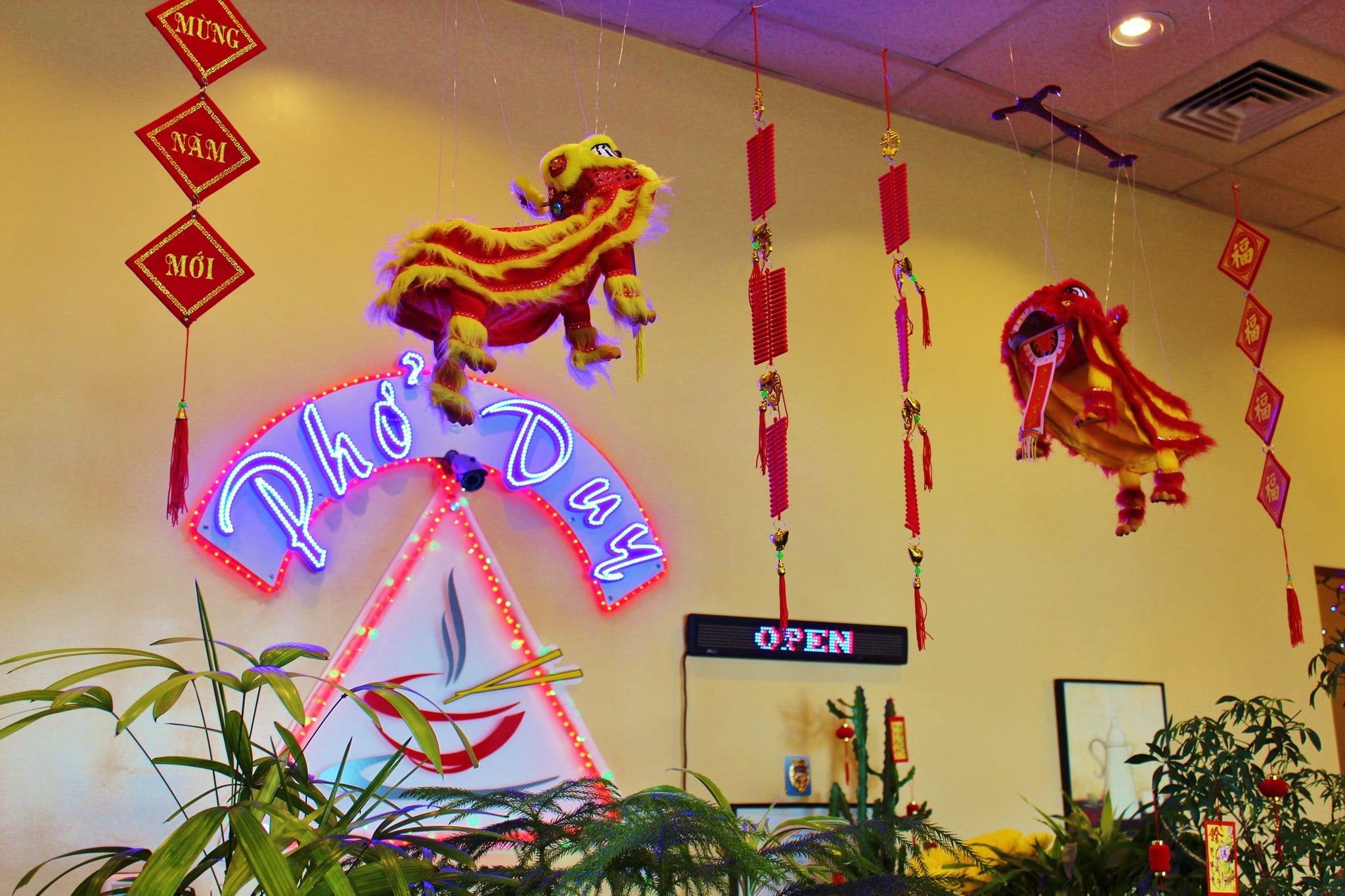 Interior of Vietnamese restaurant with neon sign, hanging decorations, and festive lion dance figures.