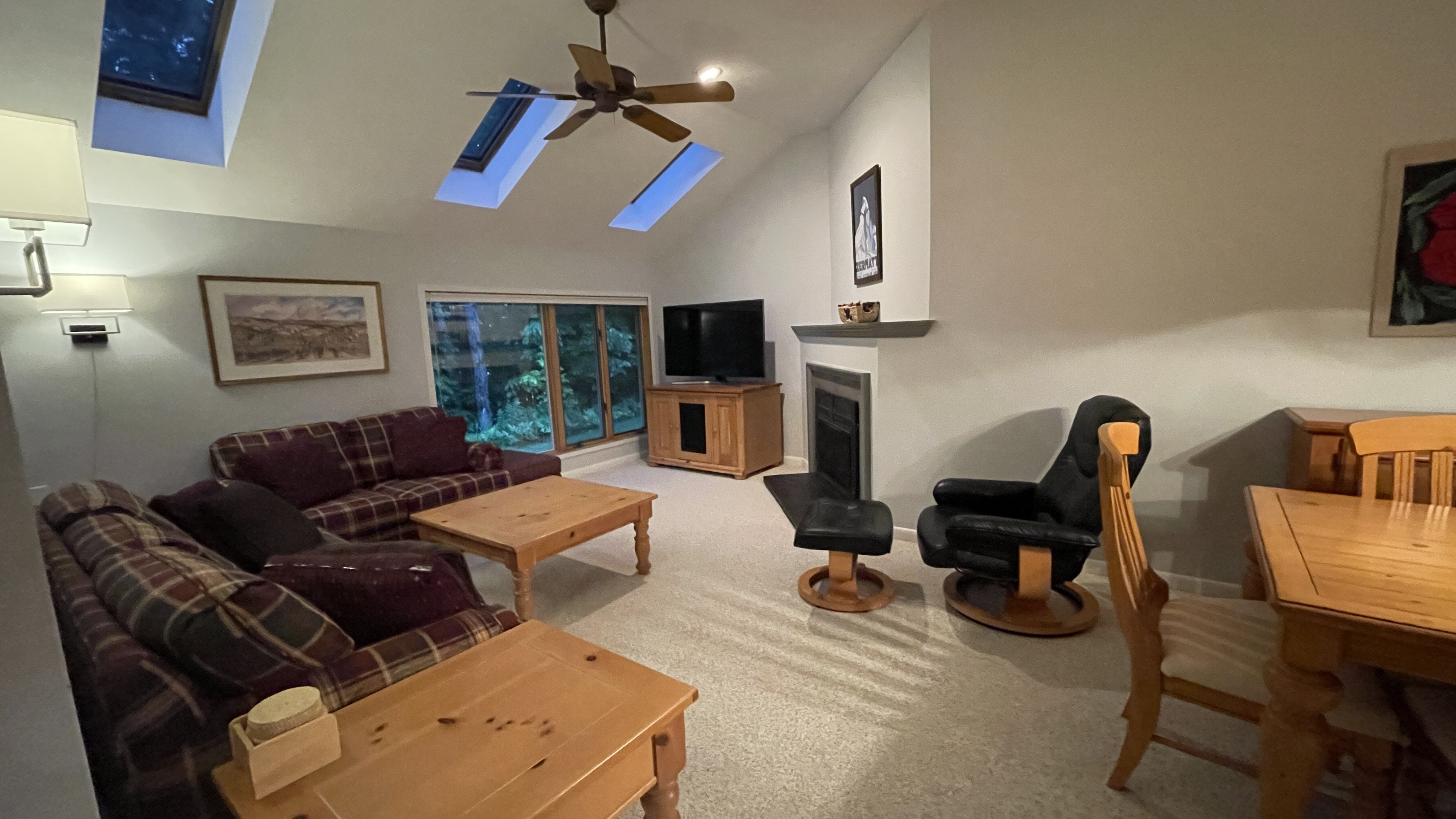Cozy living room with plaid sofas, wooden furniture, skylights, and a fireplace.