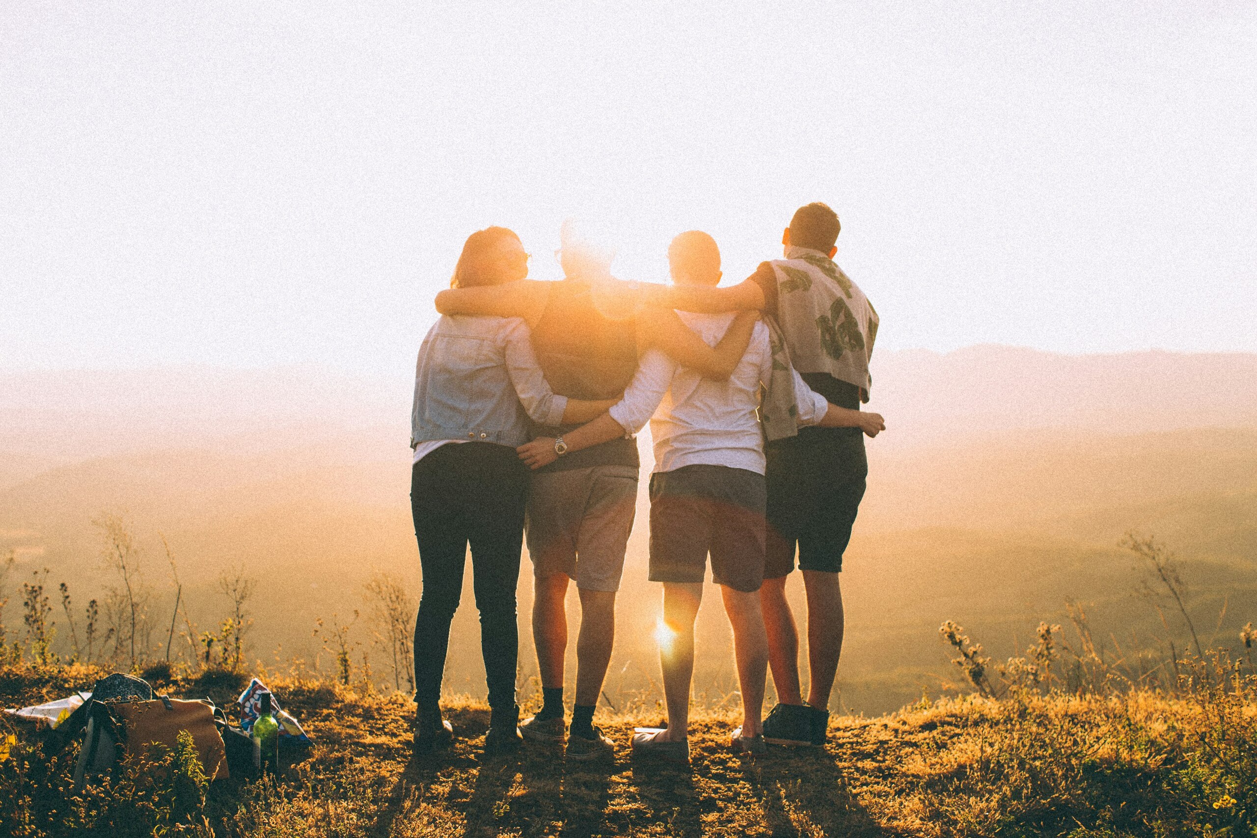 Grupo de amigos abrazados mirando el atardecer en una colina.