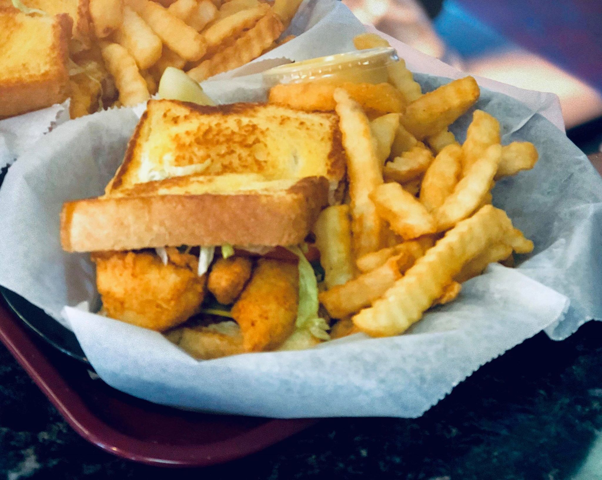 Fried fish sandwich with lettuce on toasted bread, served with crinkle-cut fries.