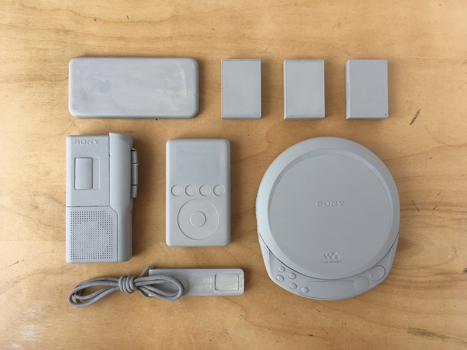 Eight Sony and Apple personal devices and micro cassette tapes painted grey.