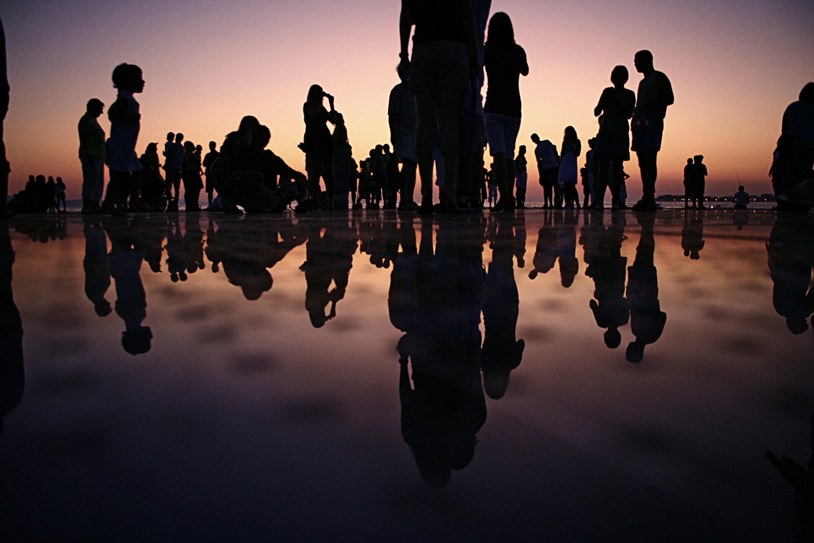 Silhouettes of people gathered at sunset, reflected on a wet surface.