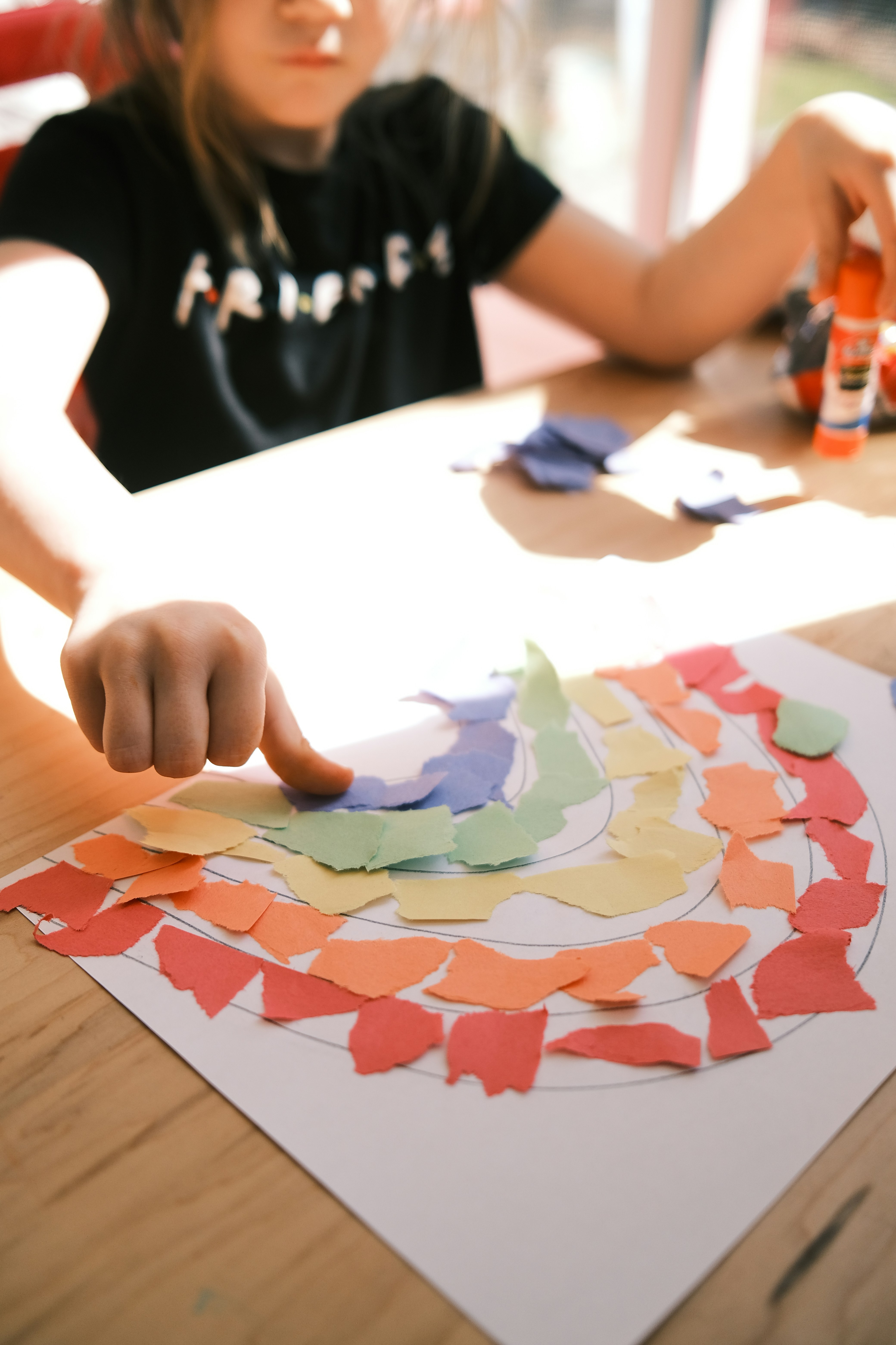 Niño haciendo manualidad con papel de colores y pegamento en una mesa escolar