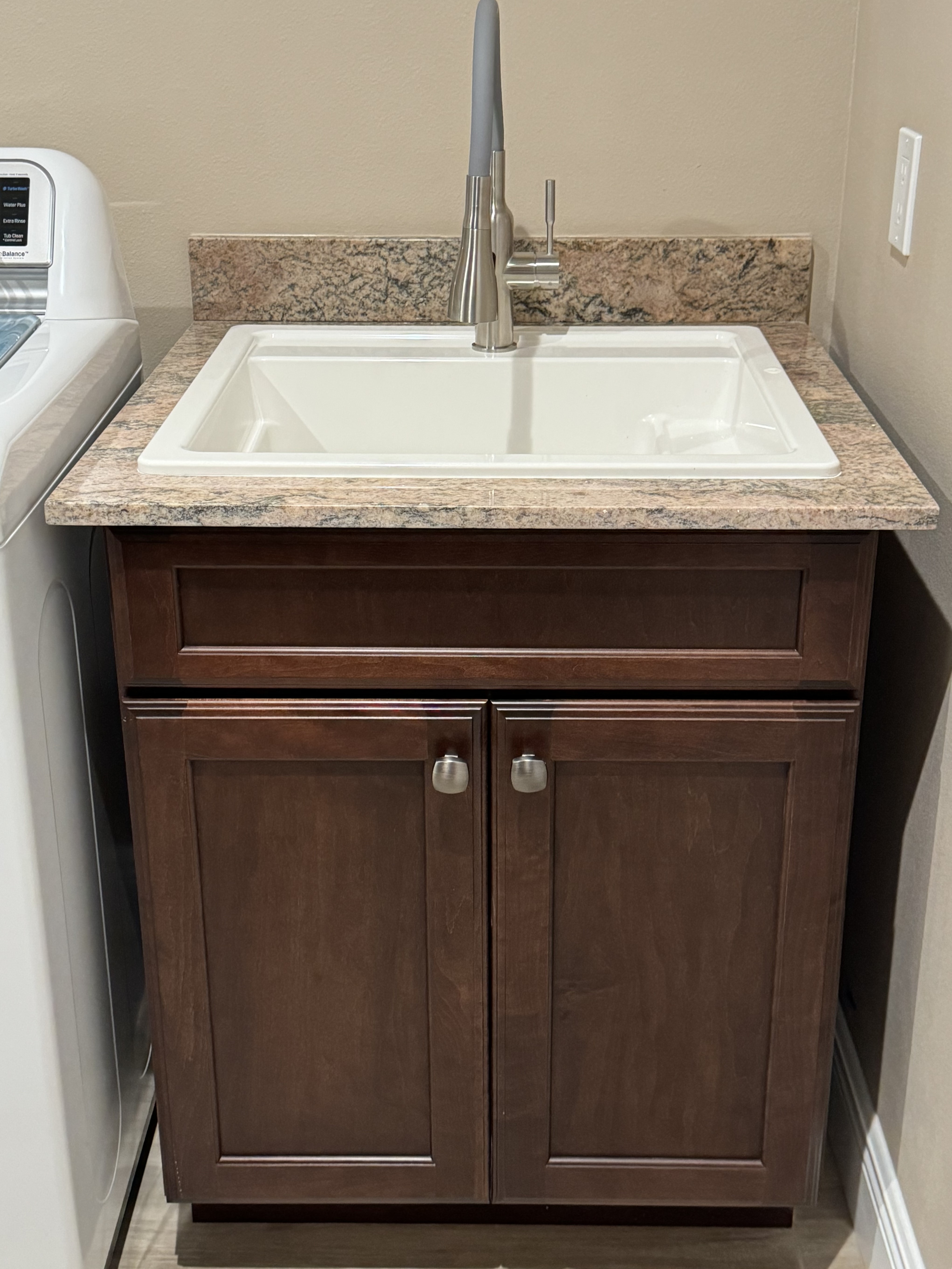Laundry room cabinetry featuring brush nickel knobs, granite countertop with 4" matching backsplash, and utility sink for easy and convenience.