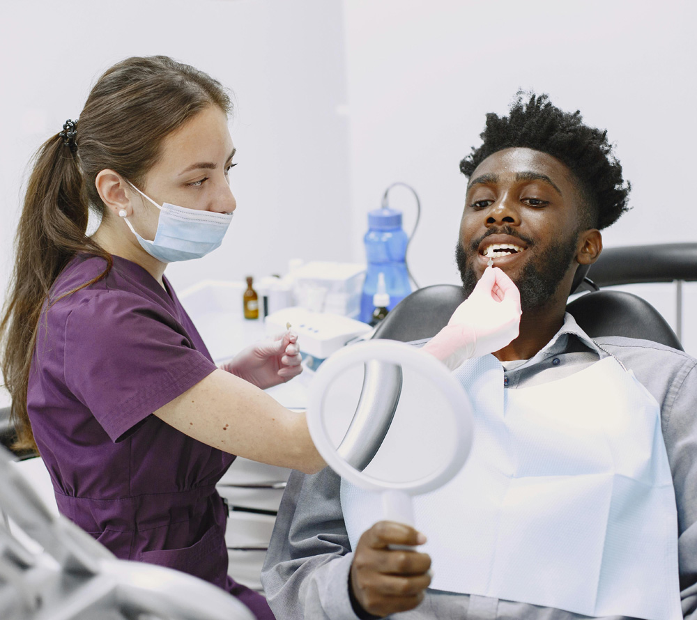 Dental hygienist working on a patient looking in a hand mirror.