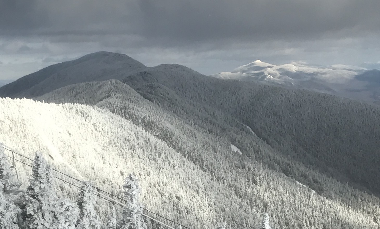 Snow-covered mountain peaks with dense pine forests under a cloudy sky.