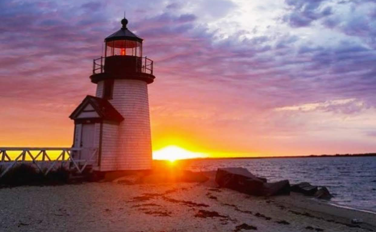 Lighthouse on a beach at sunset with vibrant purple and orange sky.