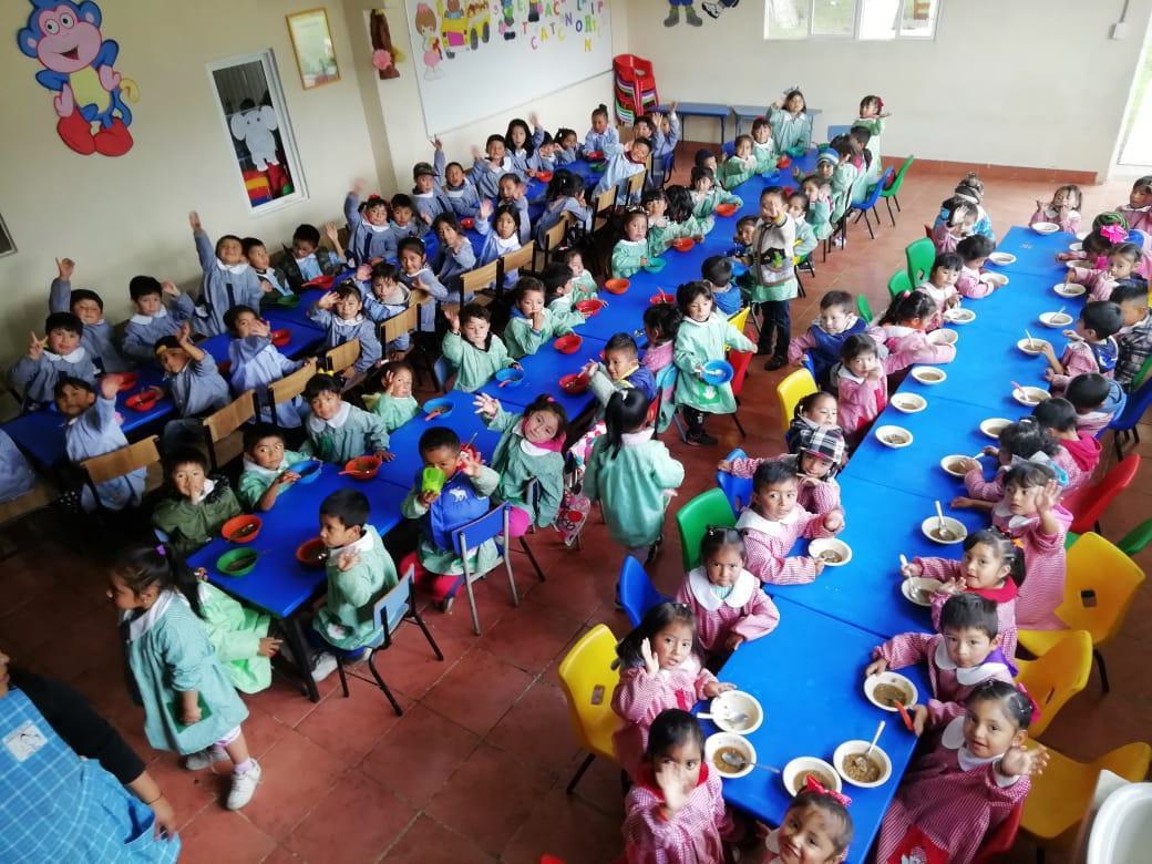 Mujer sonriendo usa tableta junto a niño con planta en interior iluminado, rodeados de vegetación y un robot.