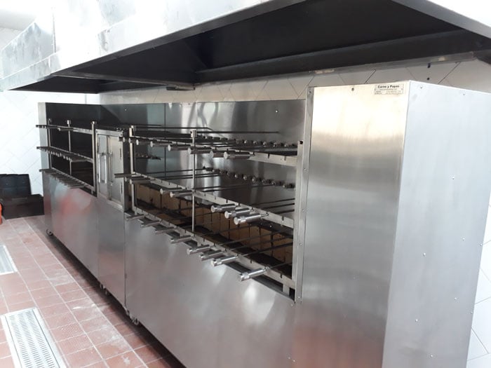 Asador industrial en cocina, construido en acero inoxidable con varias filas de varillas para asar.