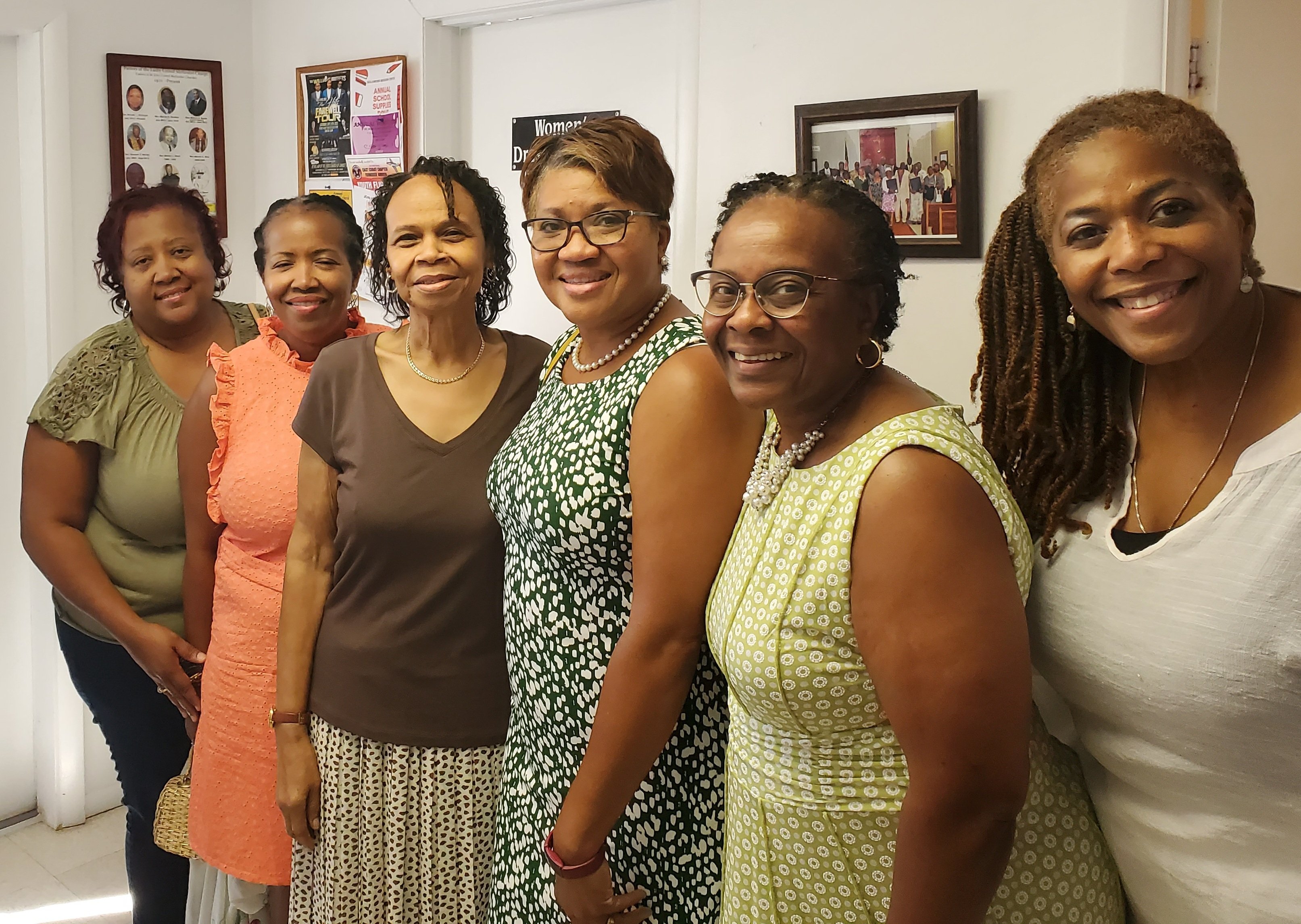 Group of six smiling women standing together indoors.