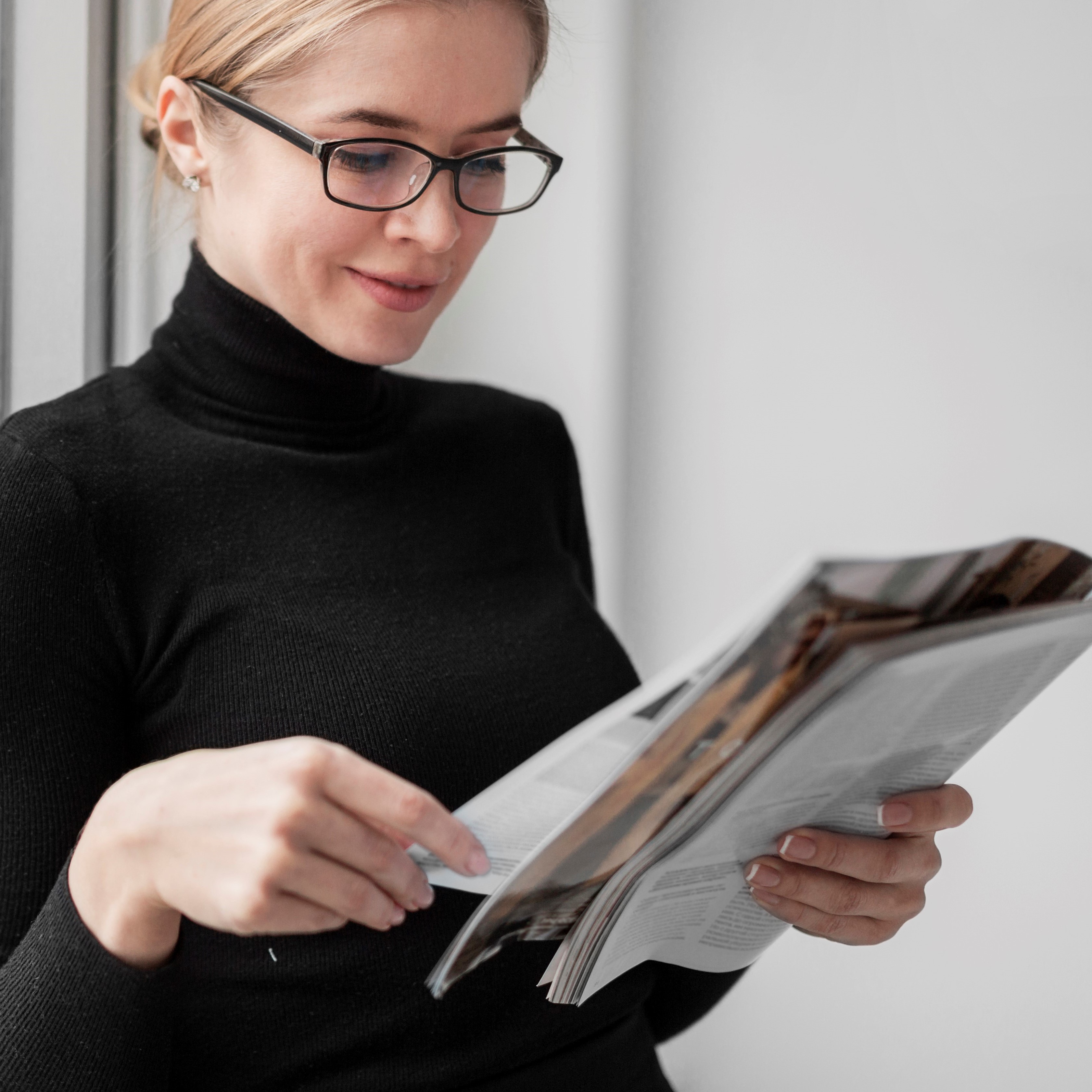 Modern open-plan office space with large windows, natural light, and employees working at desks surrounded by green plants.