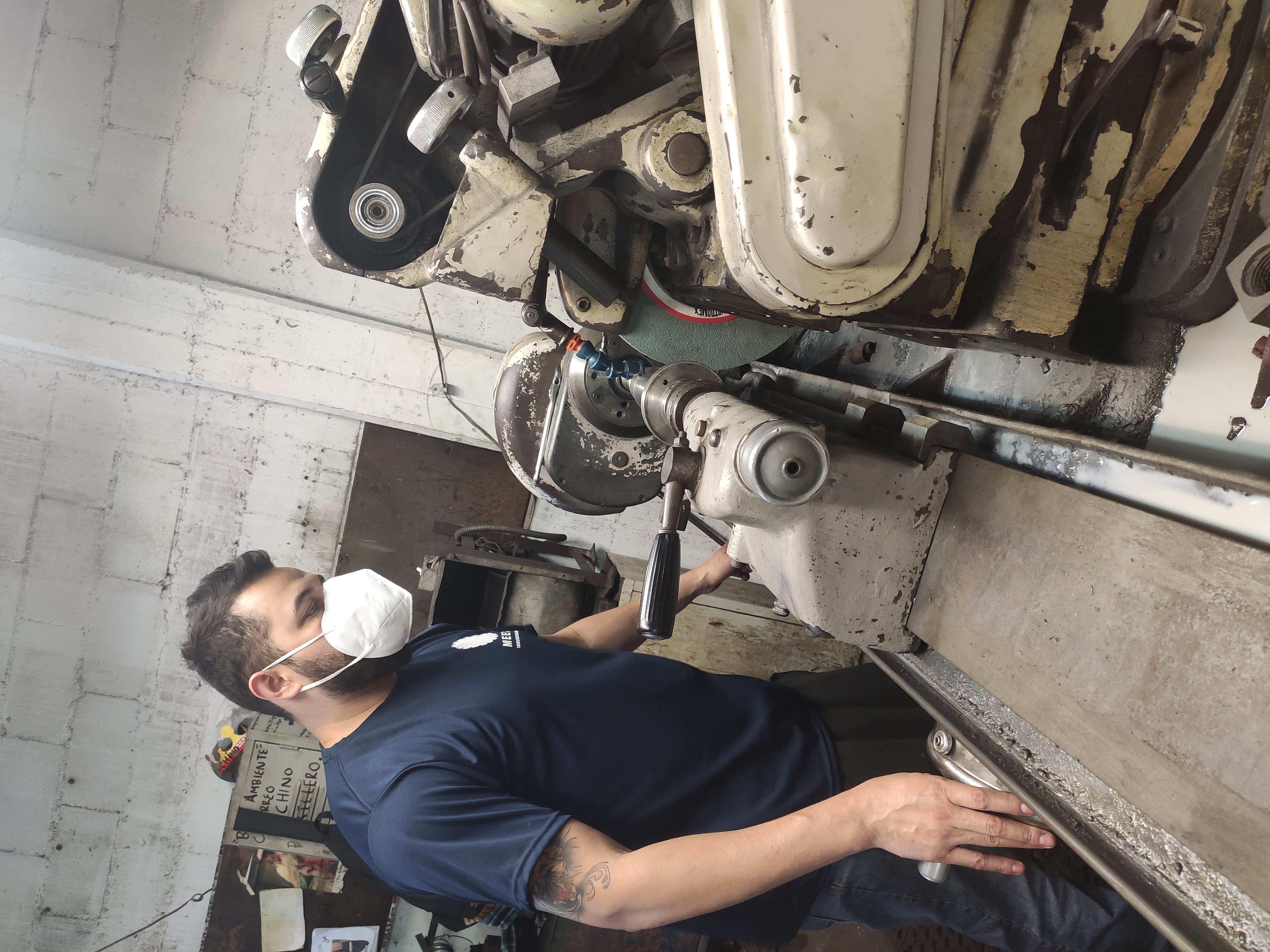 Operario usando torno en taller, llevando mascarilla protectora.