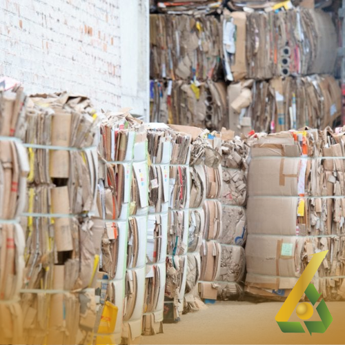 Pilas de cartón reciclado apiladas en un almacén, listas para su procesamiento.