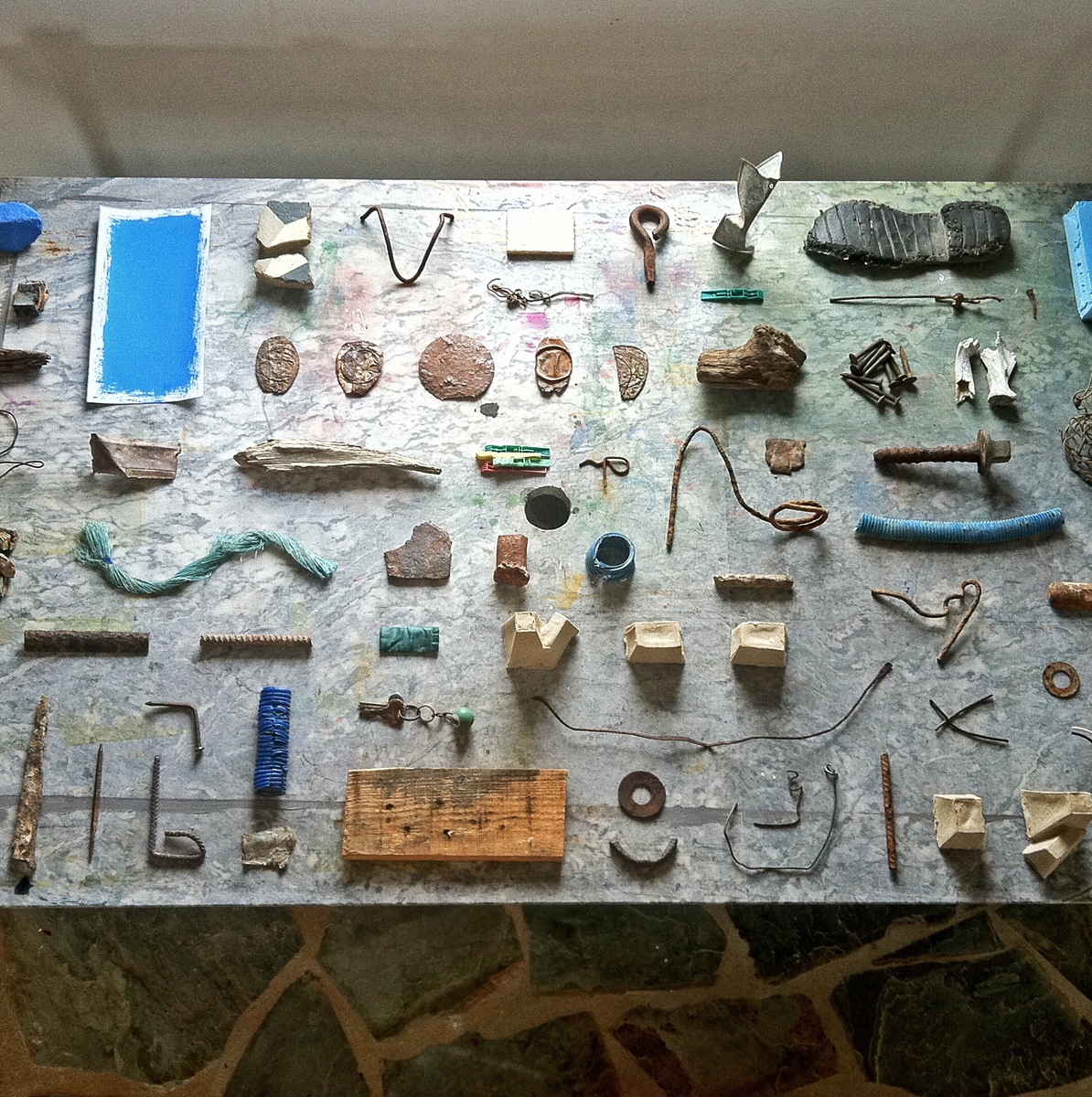 Dozens of rustic found objects, plus a minimalist blue painting, on a stone table.