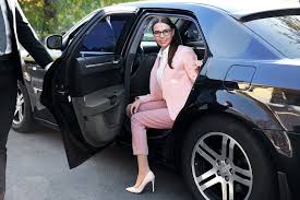Woman in pink suit exiting a black car wearing glasses and high heels.