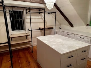 Stylish modern closet with black metal racks, wooden shelves, a central storage island, and a chandelier under sloped ceiling.