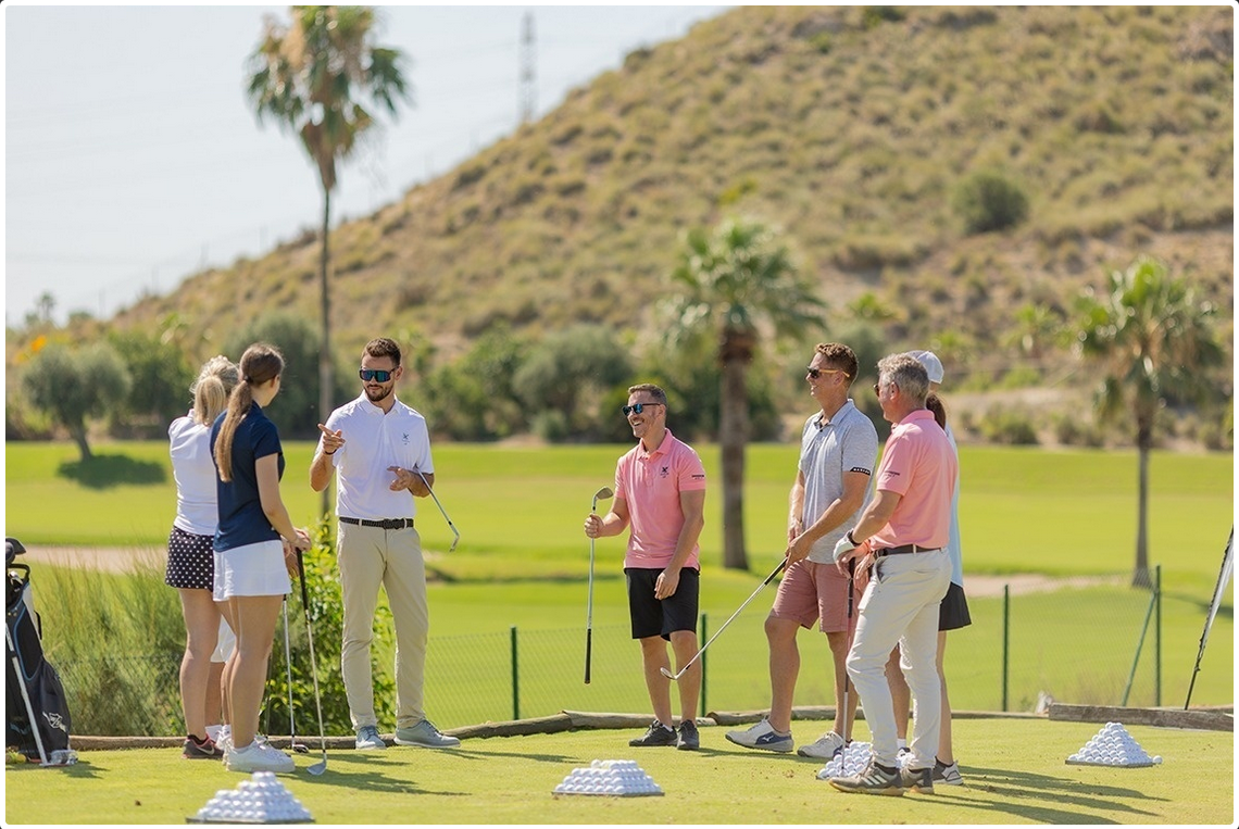 Golf club, ball, and cap on green grass by a water hazard with a scenic golf course background.