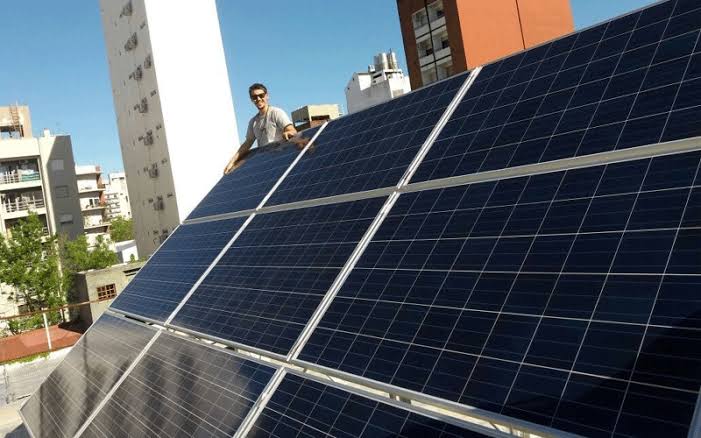 Persona instalando paneles solares en un techo con edificios de ciudad al fondo. Persona instalando paneles solares en un techo con edificios de ciudad al fondo.